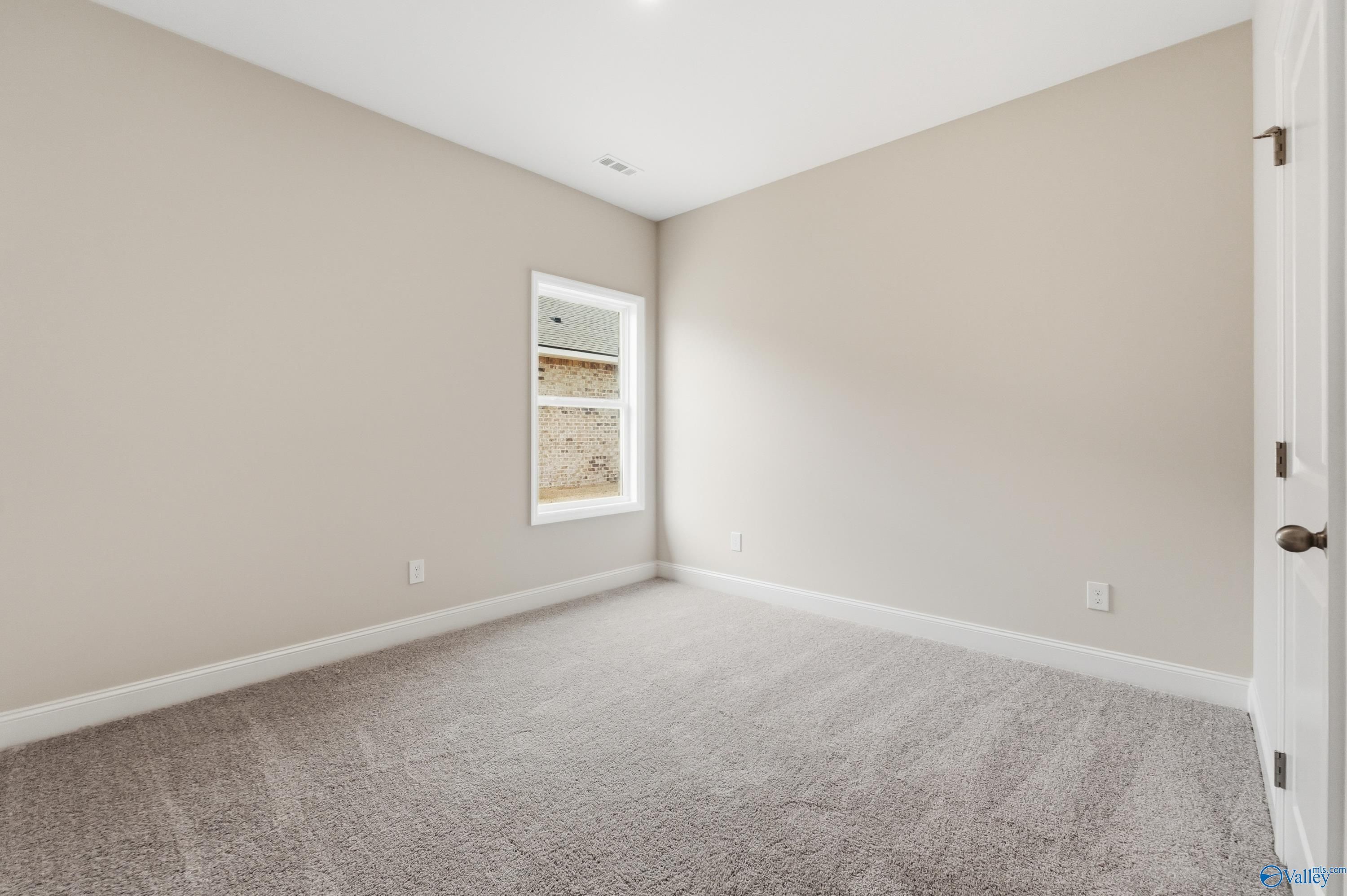 Spacious empty bedroom with beige walls, large window, and carpeted floor in Davidson Homes The Franklin, Meridianville, Alabama