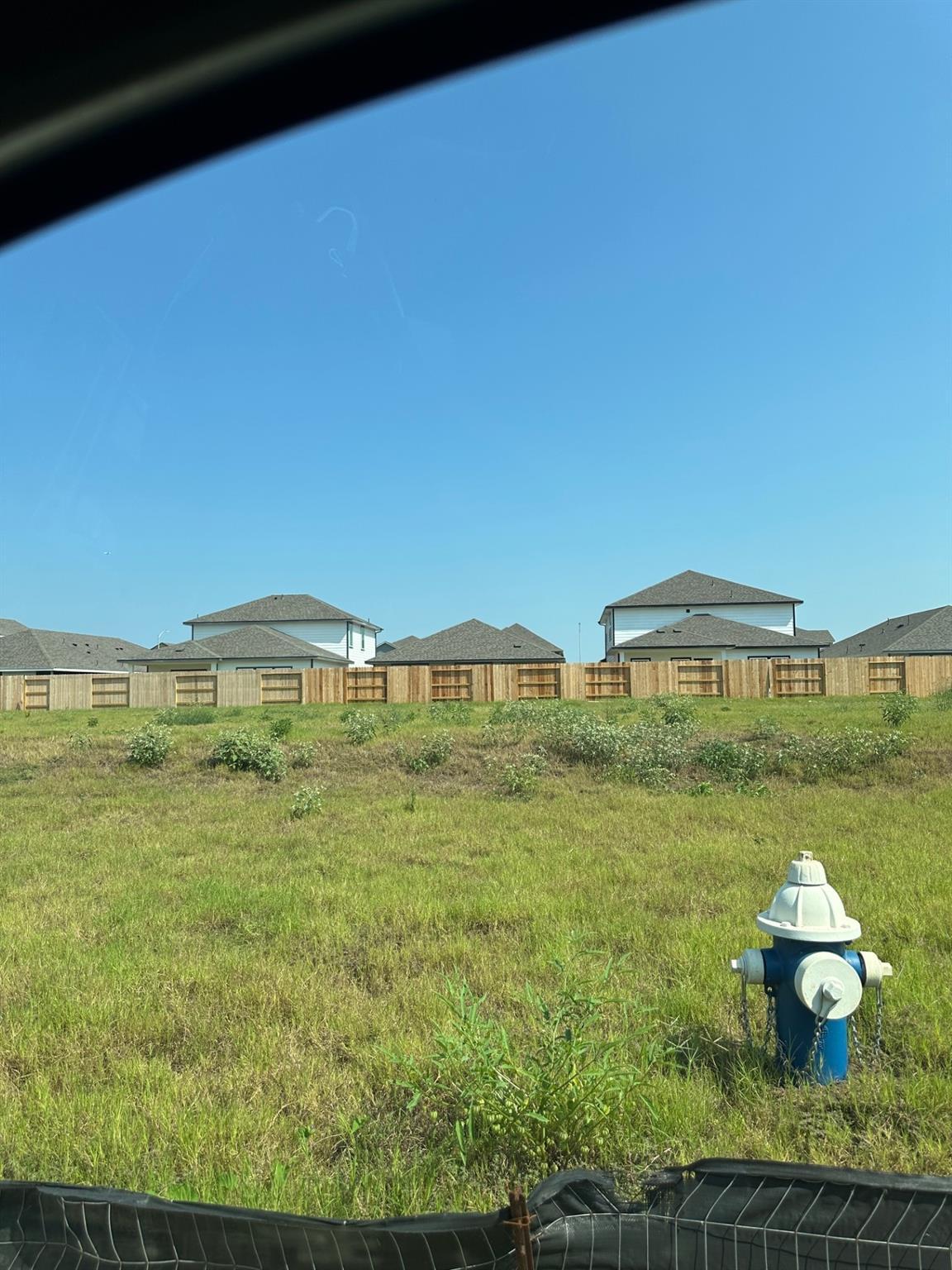 Scenic neighborhood of single-story homes behind wooden fence in Sundance Cove, Crosby, Texas, with grassy field and fire hydrant