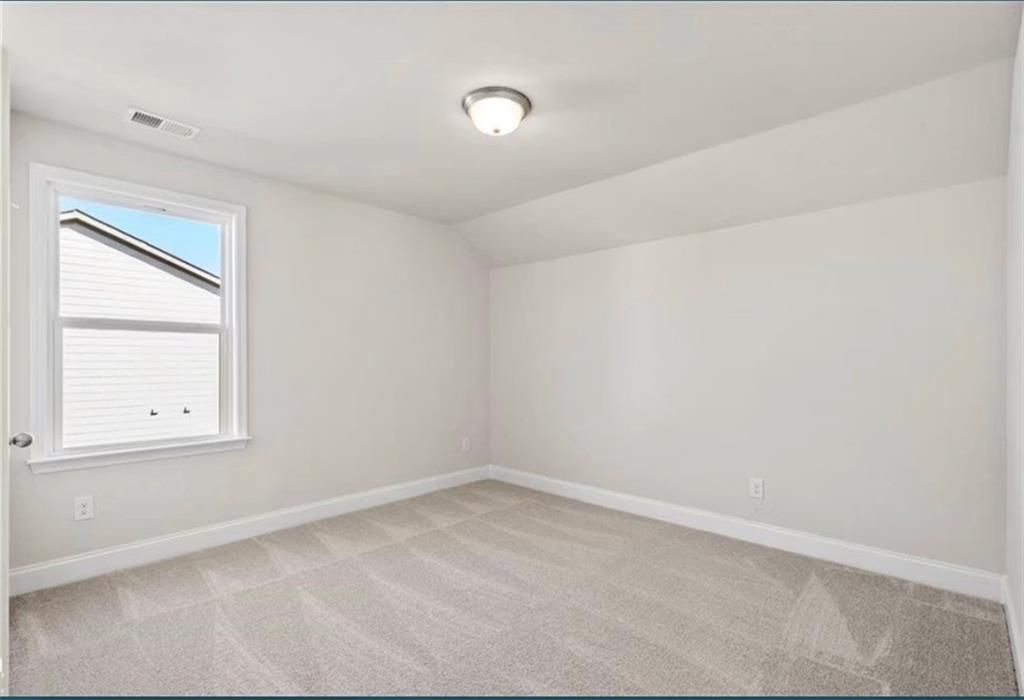 Bright, carpeted bedroom with neutral walls in The Ash C floor plan at Wehunt Meadows, Hoschton, Georgia.