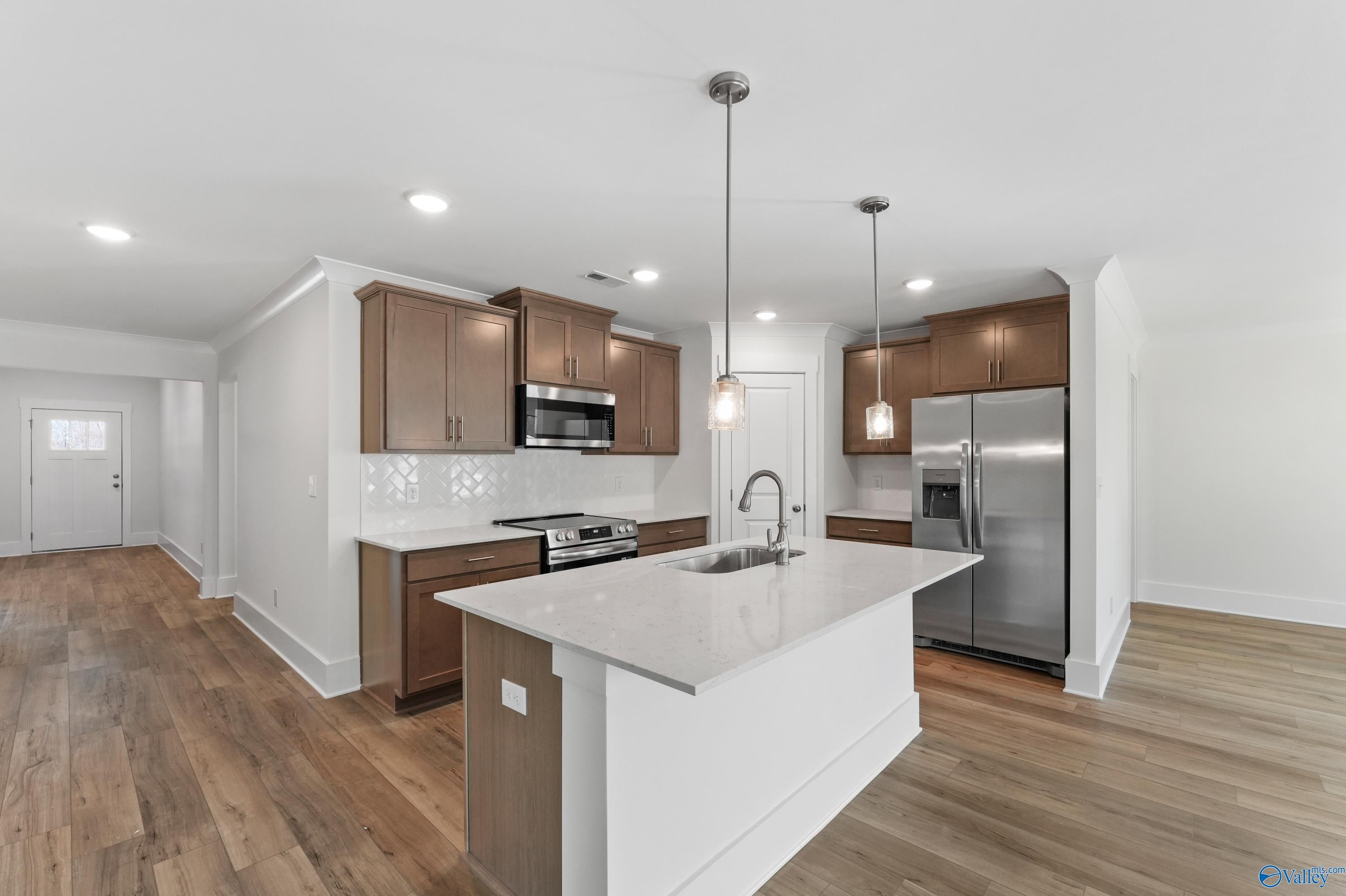 Modern kitchen with white quartz island, brown cabinets, stainless steel appliances, and hardwood floors in The Daphne C home, Arab, Alabama