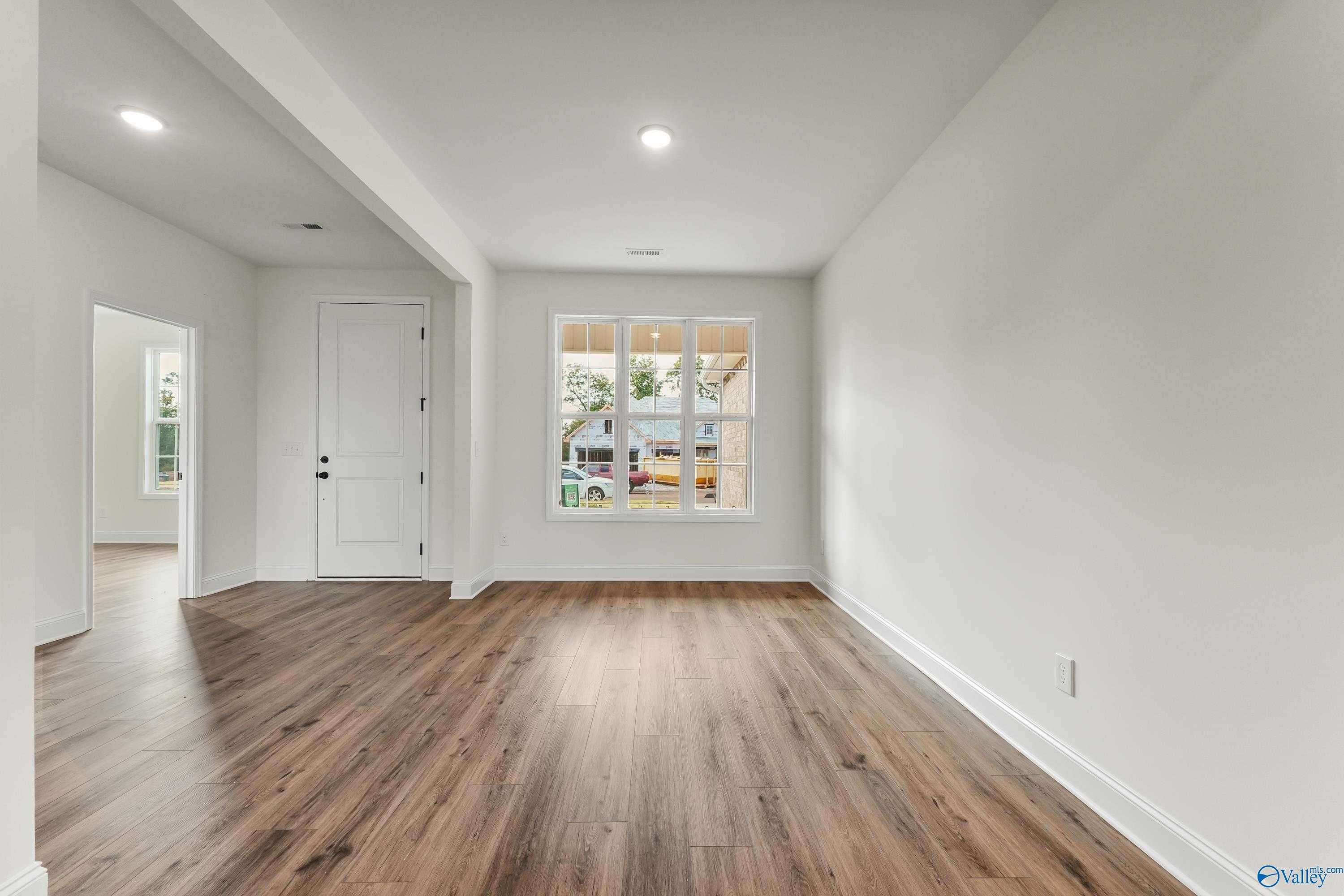 Bright open living area with warm hardwood floors, white walls, and large triple-pane window in Davidson Homes The Finleigh, Harvest, Alabama