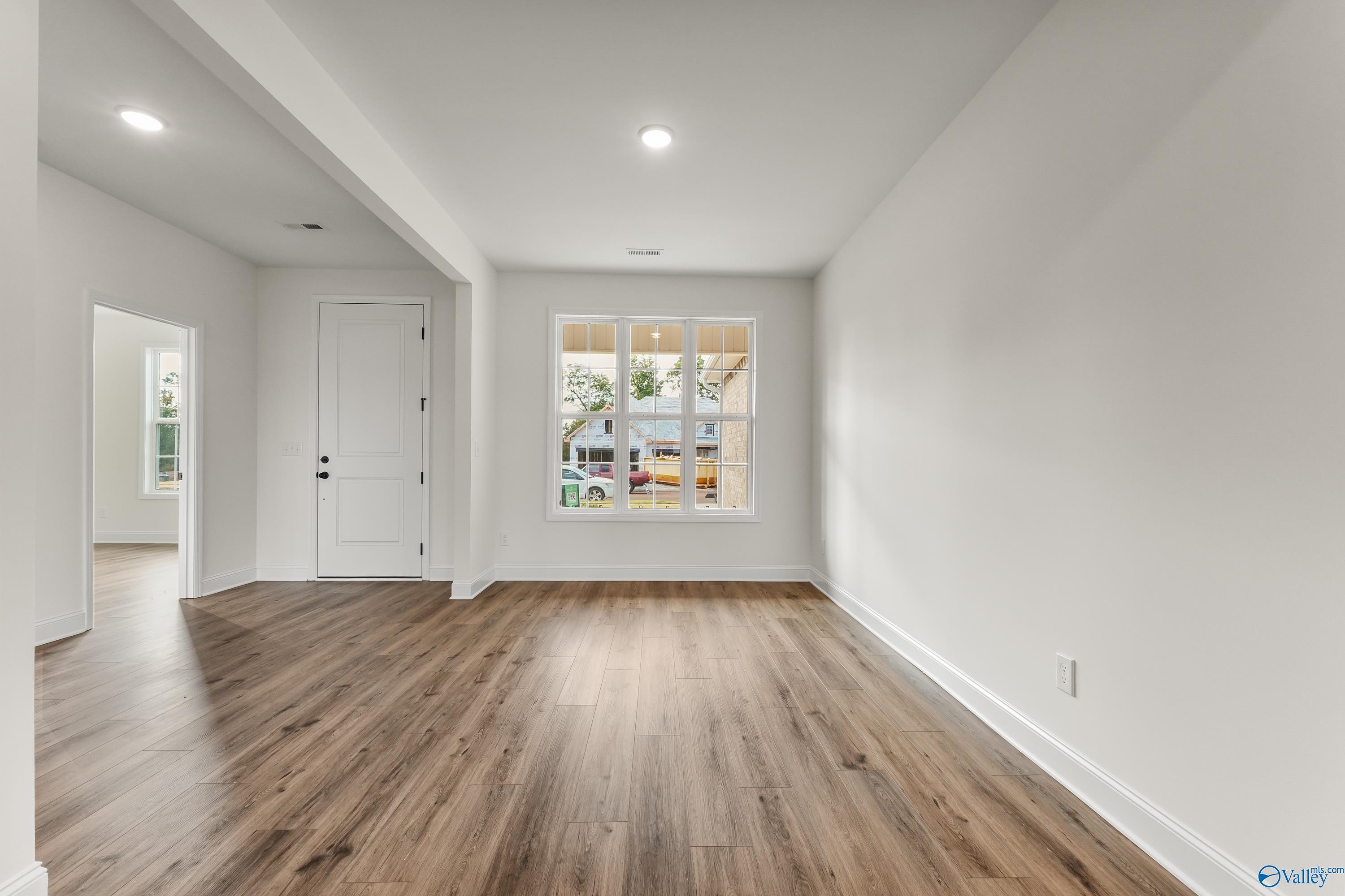 Bright open living area with warm hardwood floors, white walls, and large triple-pane window in Davidson Homes The Finleigh, Harvest, Alabama
