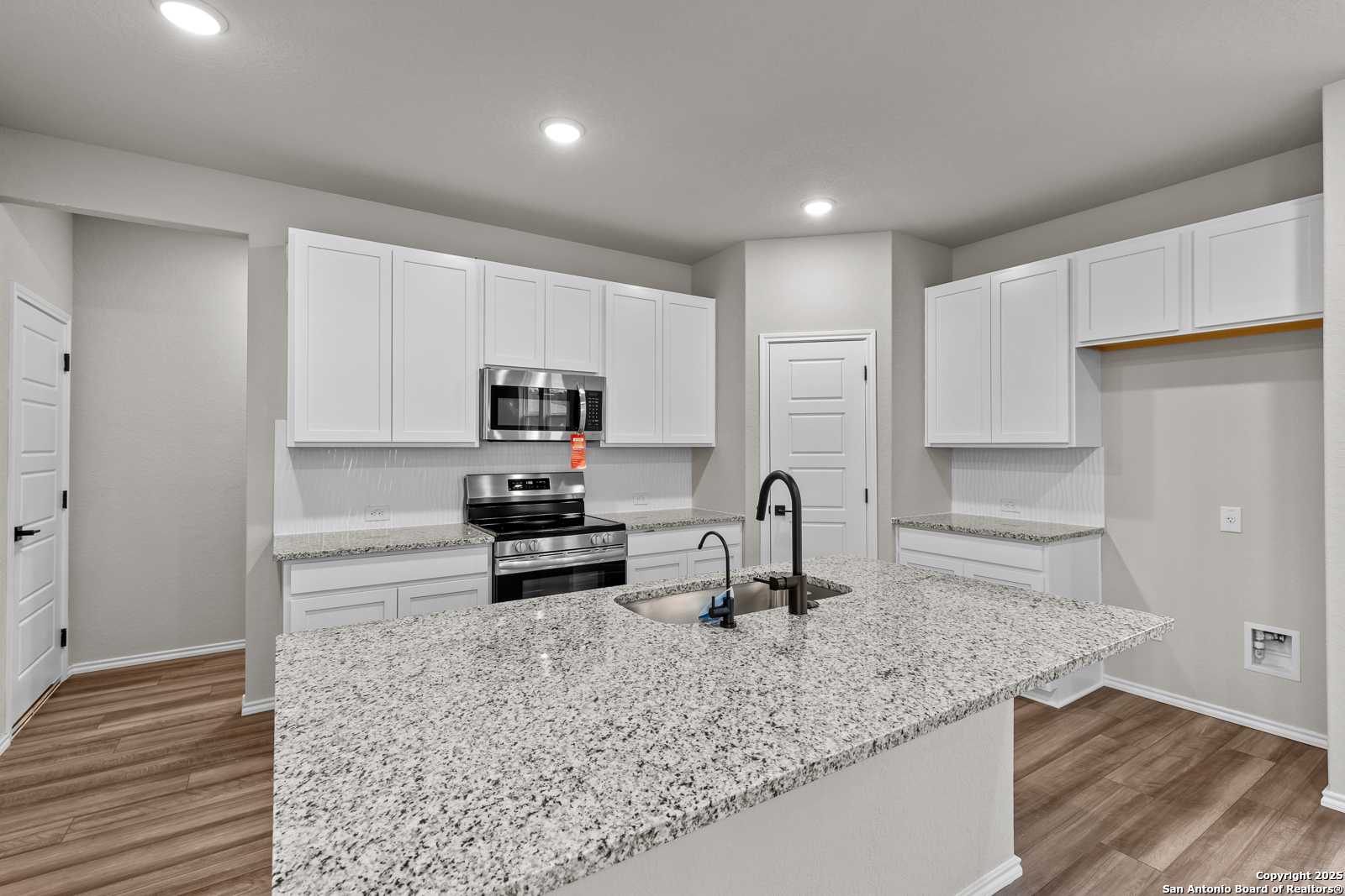 Modern kitchen with white cabinets, granite island, stainless steel appliances in Davidson Homes The Murray I, San Antonio