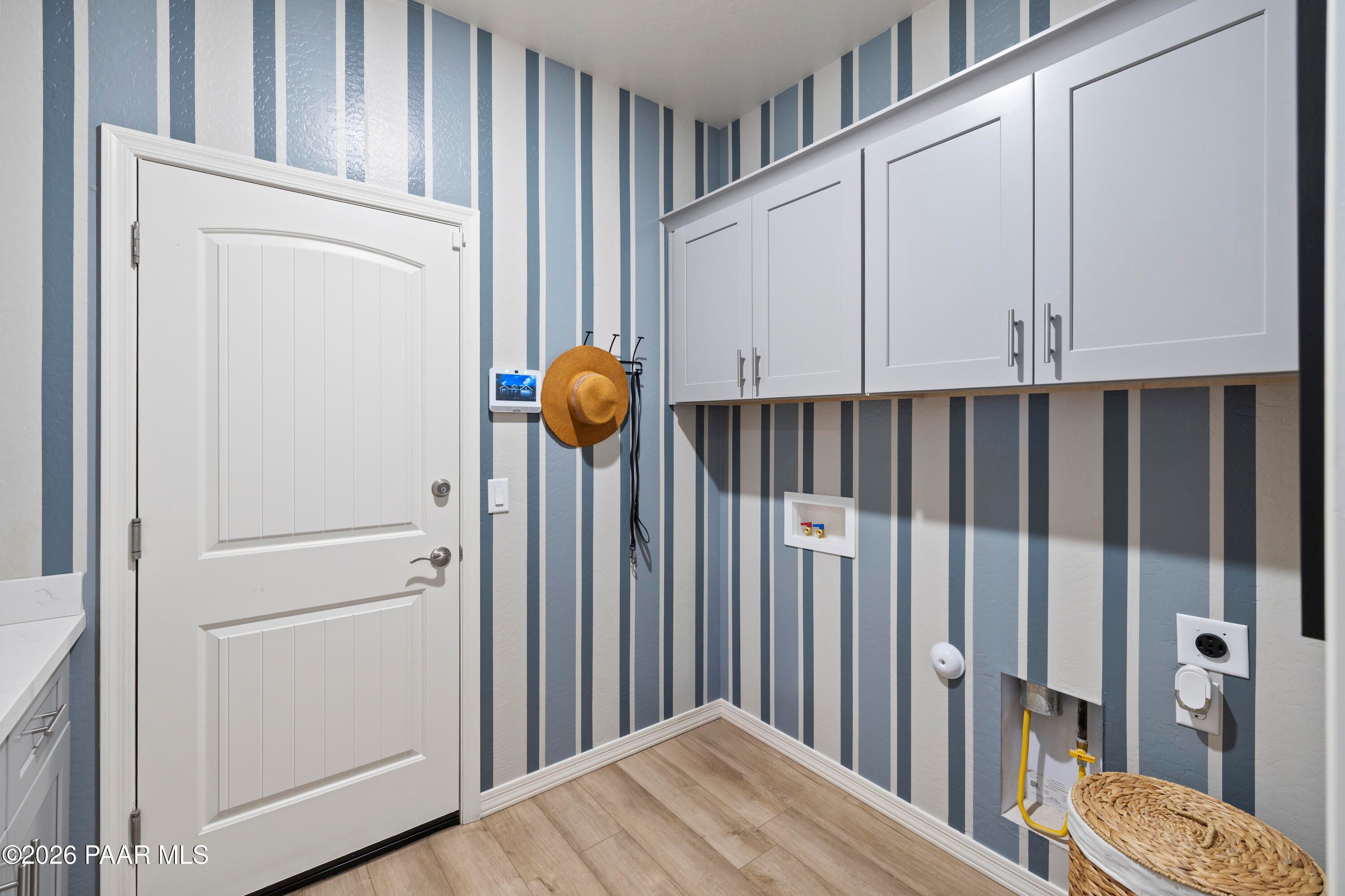 Laundry room with blue striped wallpaper, white cabinets, and wood-look flooring in The Harmony A, North Ridge, Prescott.
