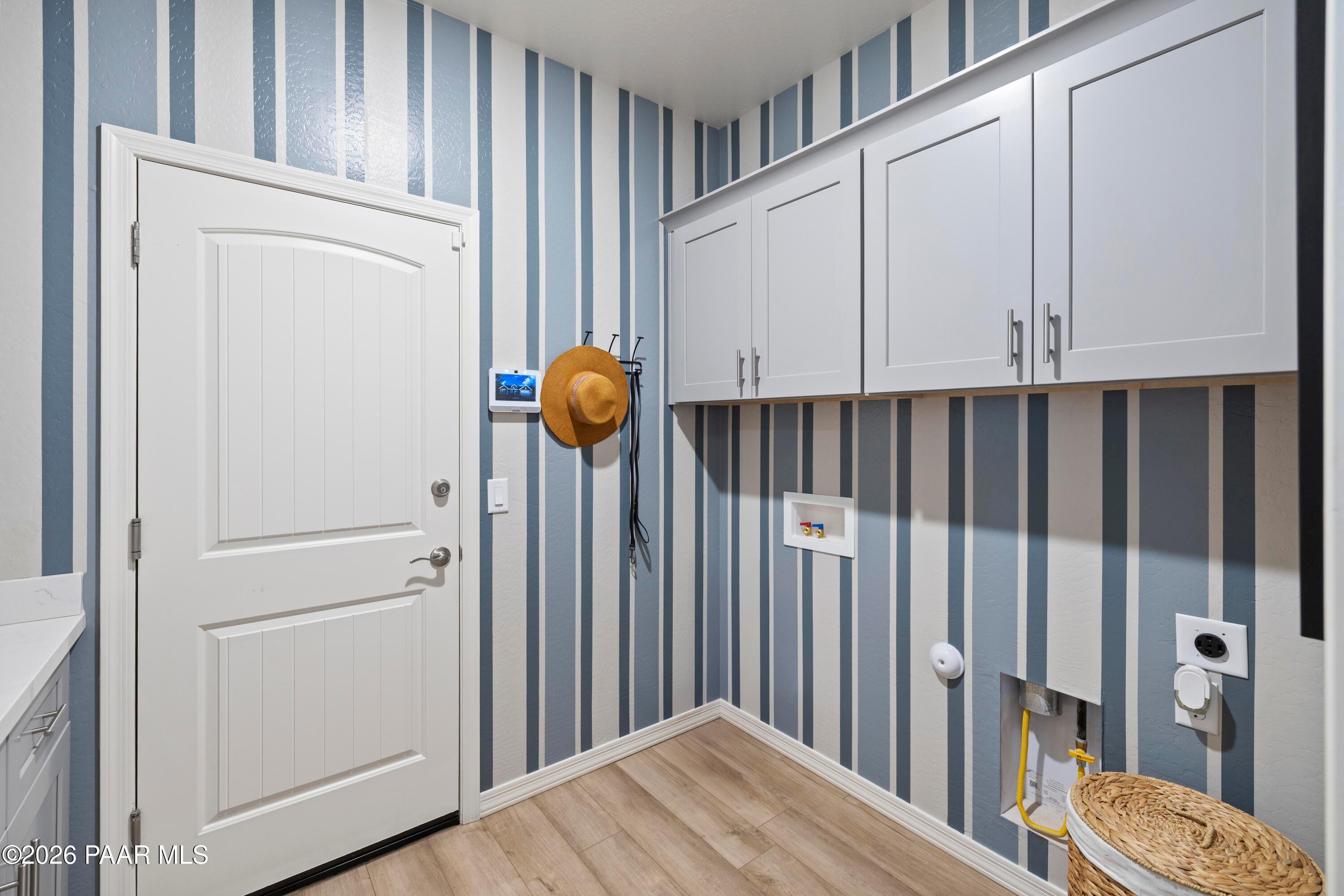 Laundry room with blue striped wallpaper, white cabinets, and wood-look flooring in The Harmony A, North Ridge, Prescott.