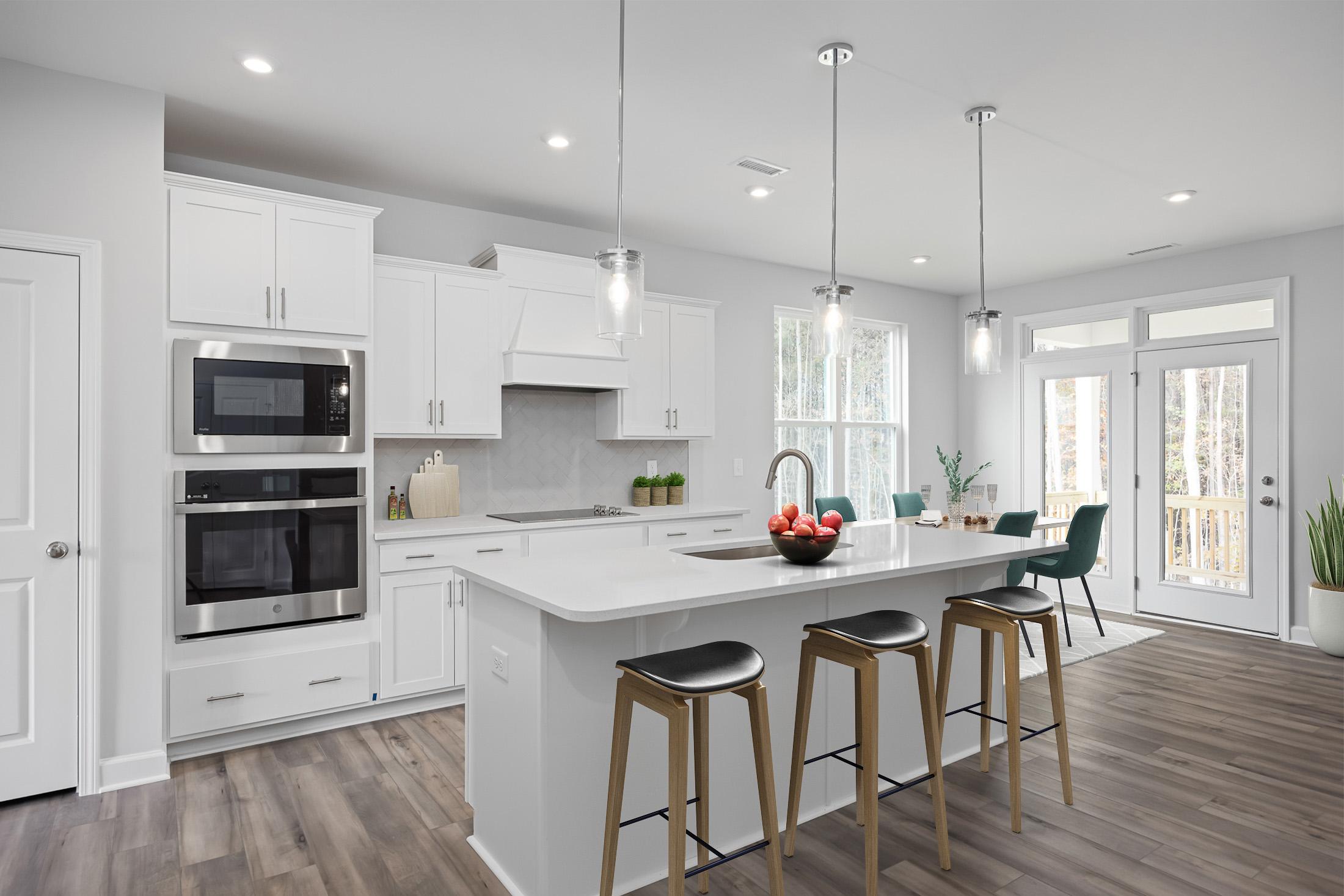 Modern kitchen at Stagecoach Corner in Mebane NC with white cabinets, stainless steel appliances, large island, bar stools, and hardwood floors
