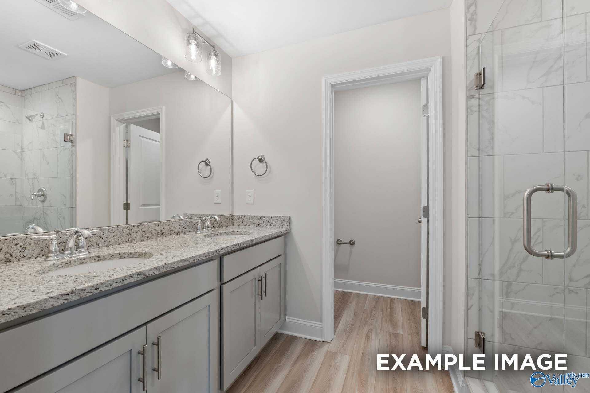 Modern master bathroom featuring double granite vanity, frameless glass shower, and hardwood floors in Davidson Homes The Camden, Huntsville AL