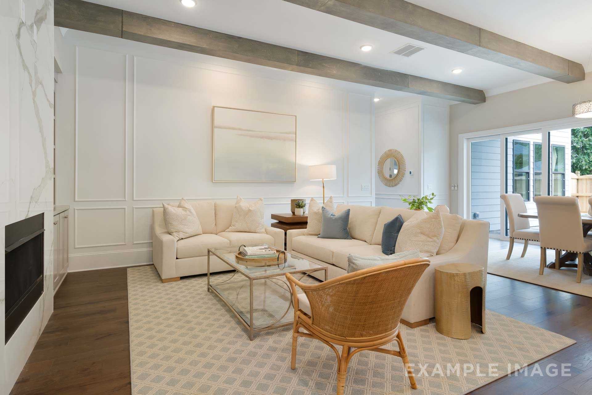 Spacious living room in The Seaside by Davidson Homes, Woodstock GA, featuring white wainscoting, neutral sofas, fireplace, and open dining area