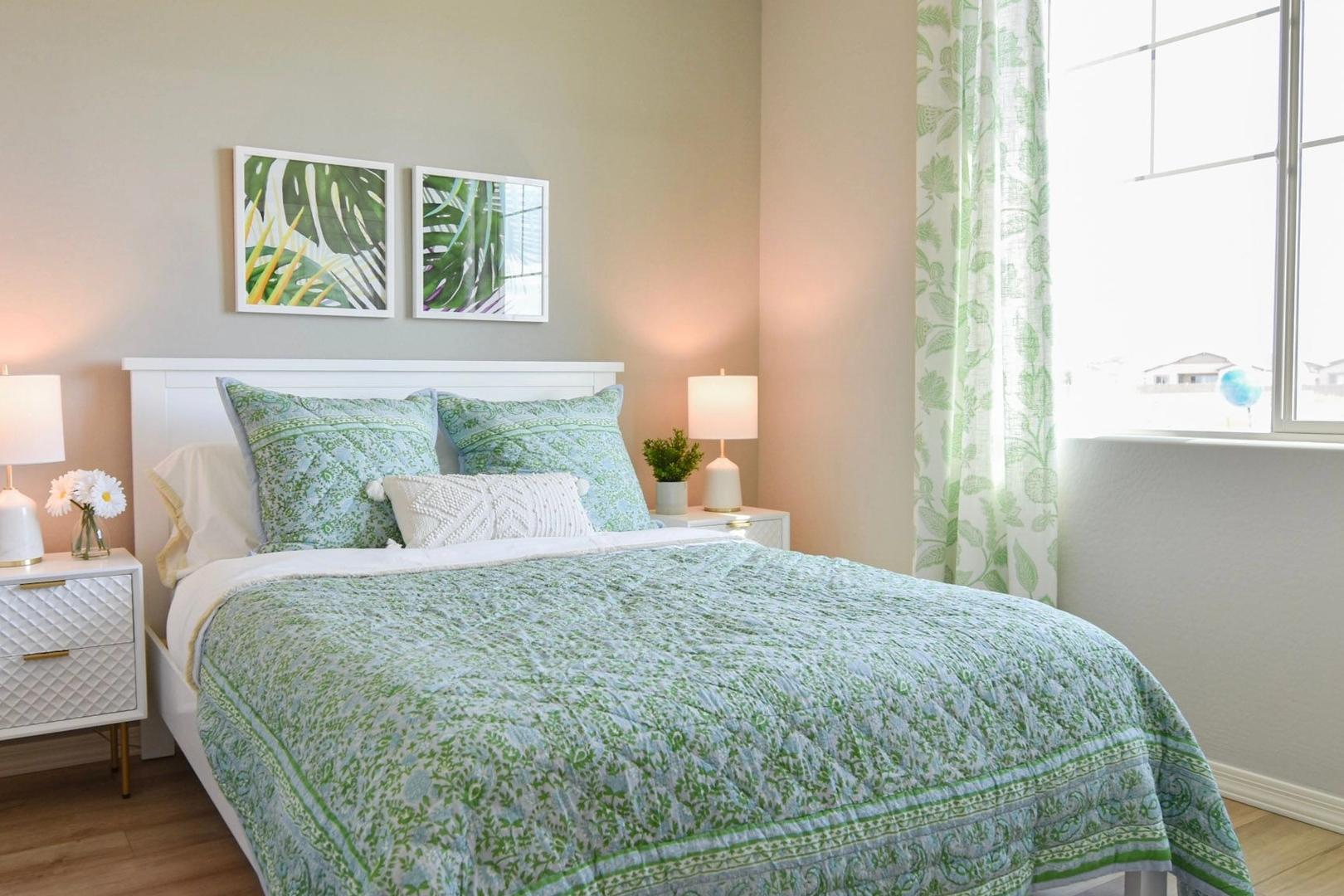 Cozy master bedroom in The Harmony B featuring green quilted king bed, tropical palm art, and sheer green curtains