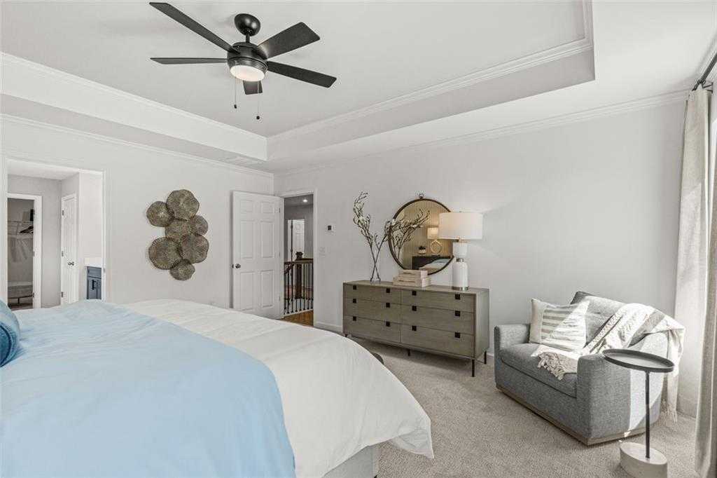 Cozy bedroom with blue-white bed, gray dresser, armchair, round mirror, and ceiling fan in Davidson Homes The Hickory B, Hoschton, GA