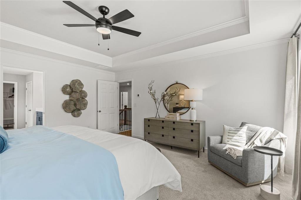 Cozy bedroom with blue-white bed, gray dresser, armchair, round mirror, and ceiling fan in Davidson Homes The Hickory B, Hoschton, GA
