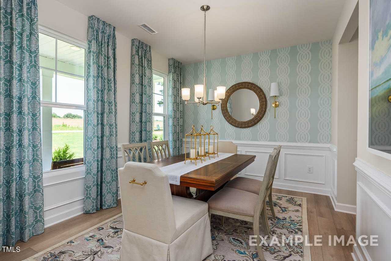 Elegant dining room featuring wooden table, blue patterned wallpaper, chandelier, and large windows in The Willow G by Davidson Homes, Angier, NC