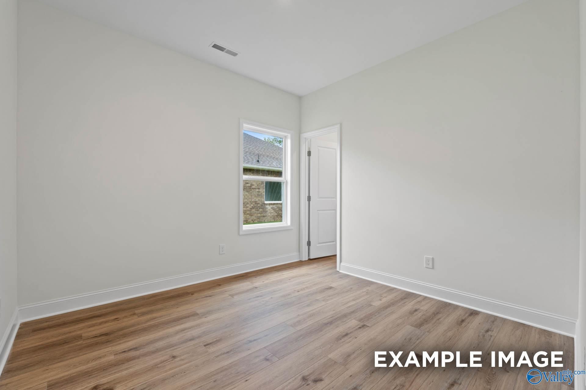Bright empty bedroom with light hardwood floors, white walls, and large window in Evermore Homes The Daphne E, Harvest, AL