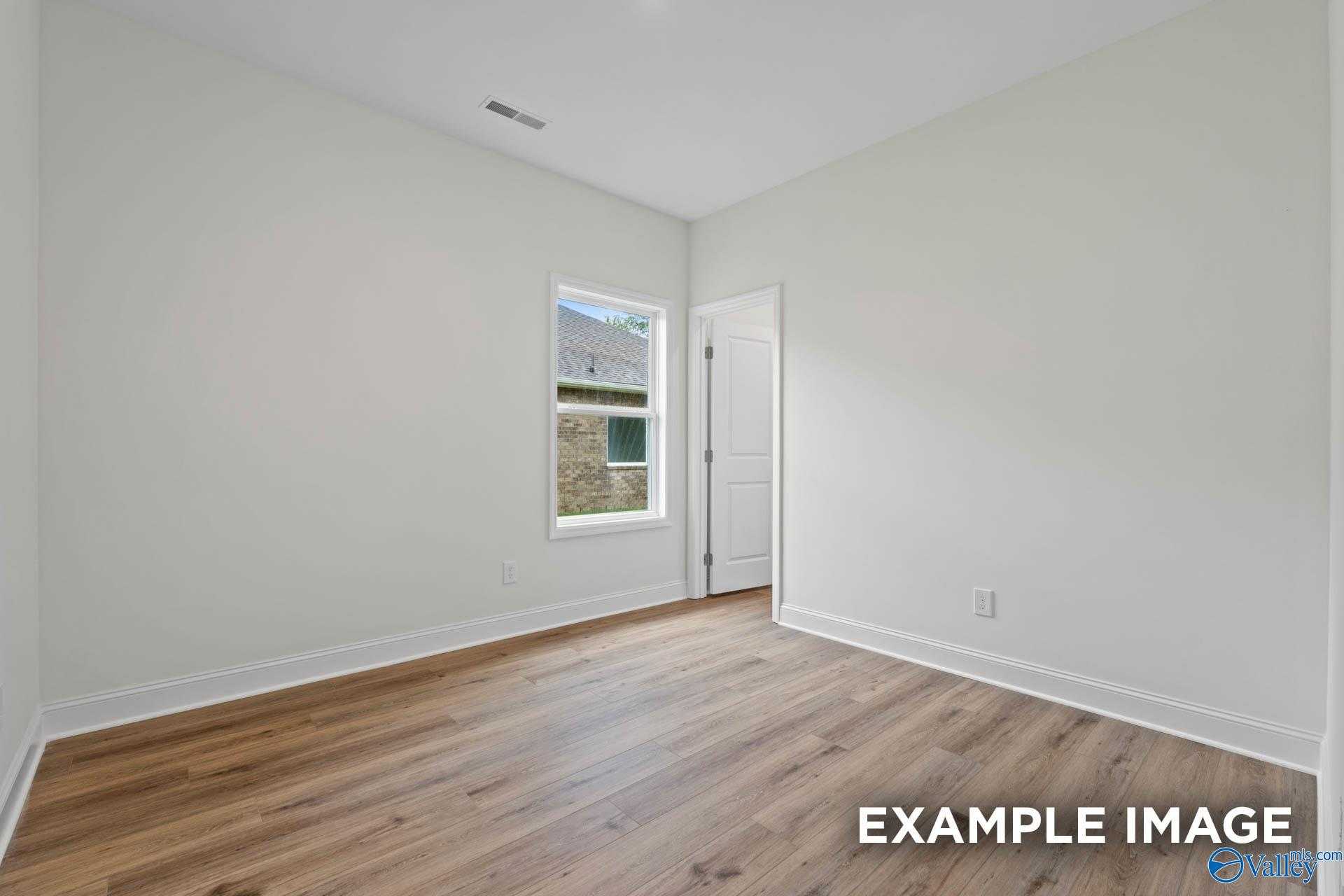 Bright empty bedroom with hardwood floors, large window, and white walls in Davidson Homes The Daphne D, Athens, Alabama