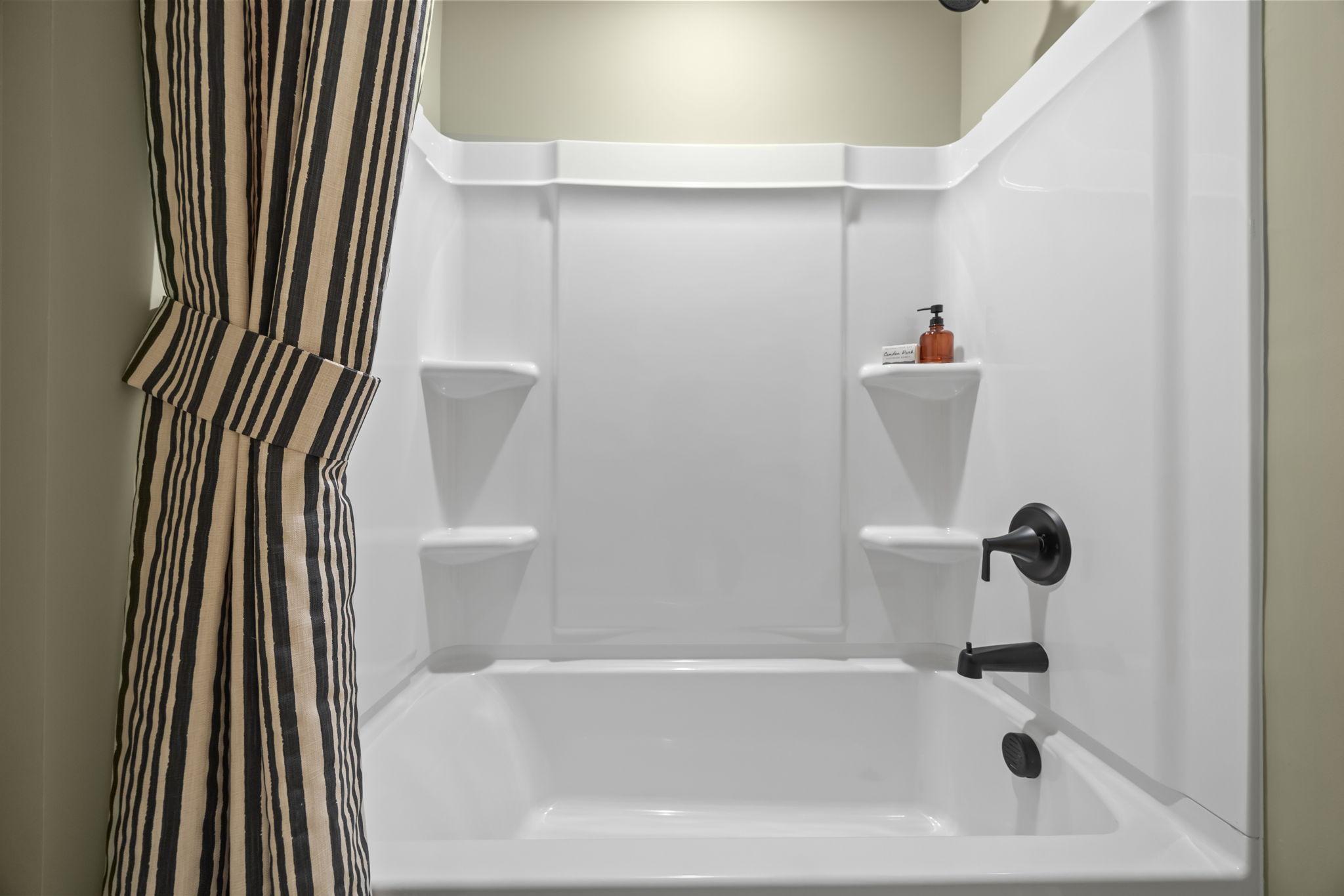 Modern tub and shower combination in The Mitchell bathroom featuring sleek matte black fixtures and a striped shower curtain.