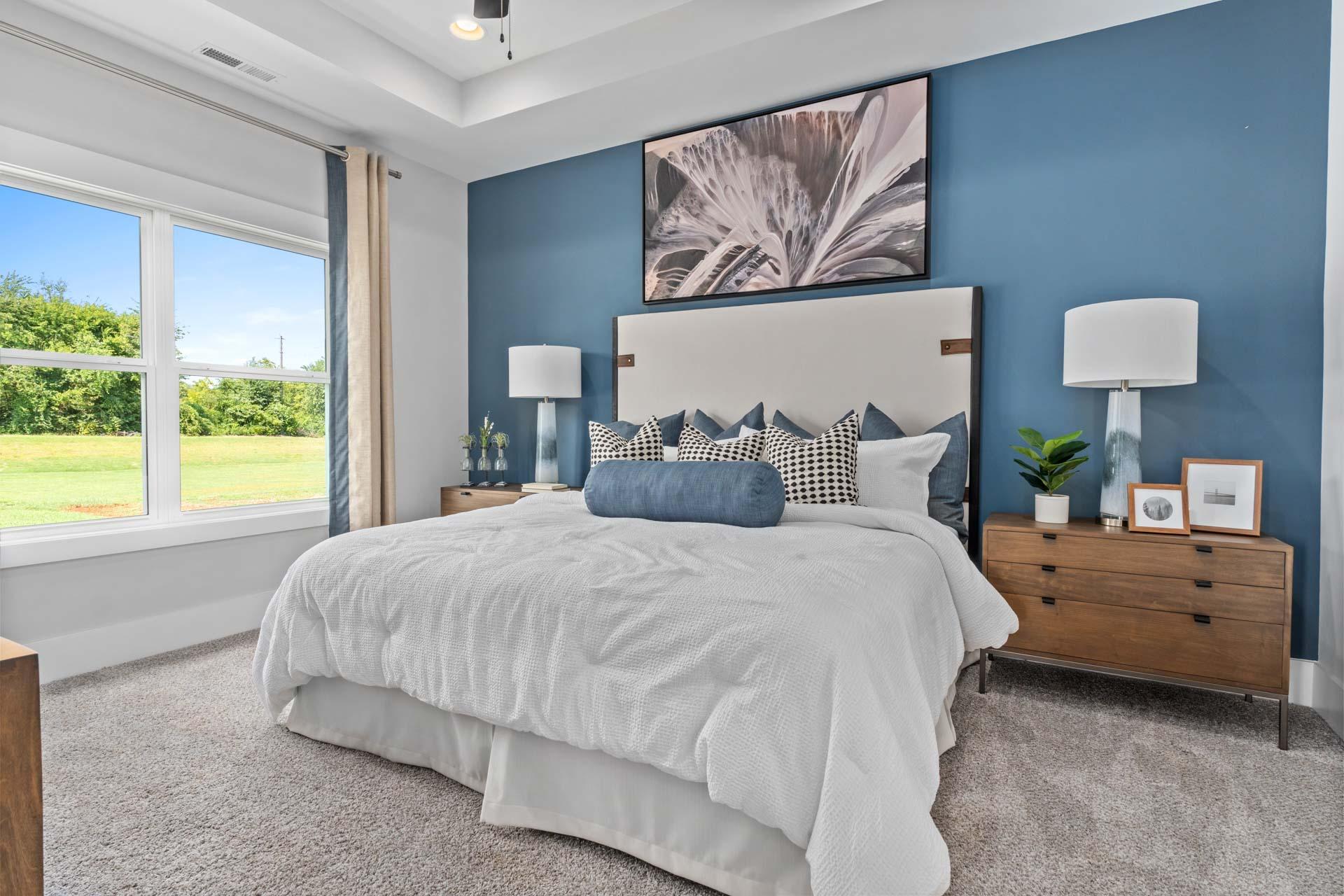 Serene master bedroom at Blue Spring in Huntsville AL with blue accent wall, king bed, and scenic window view