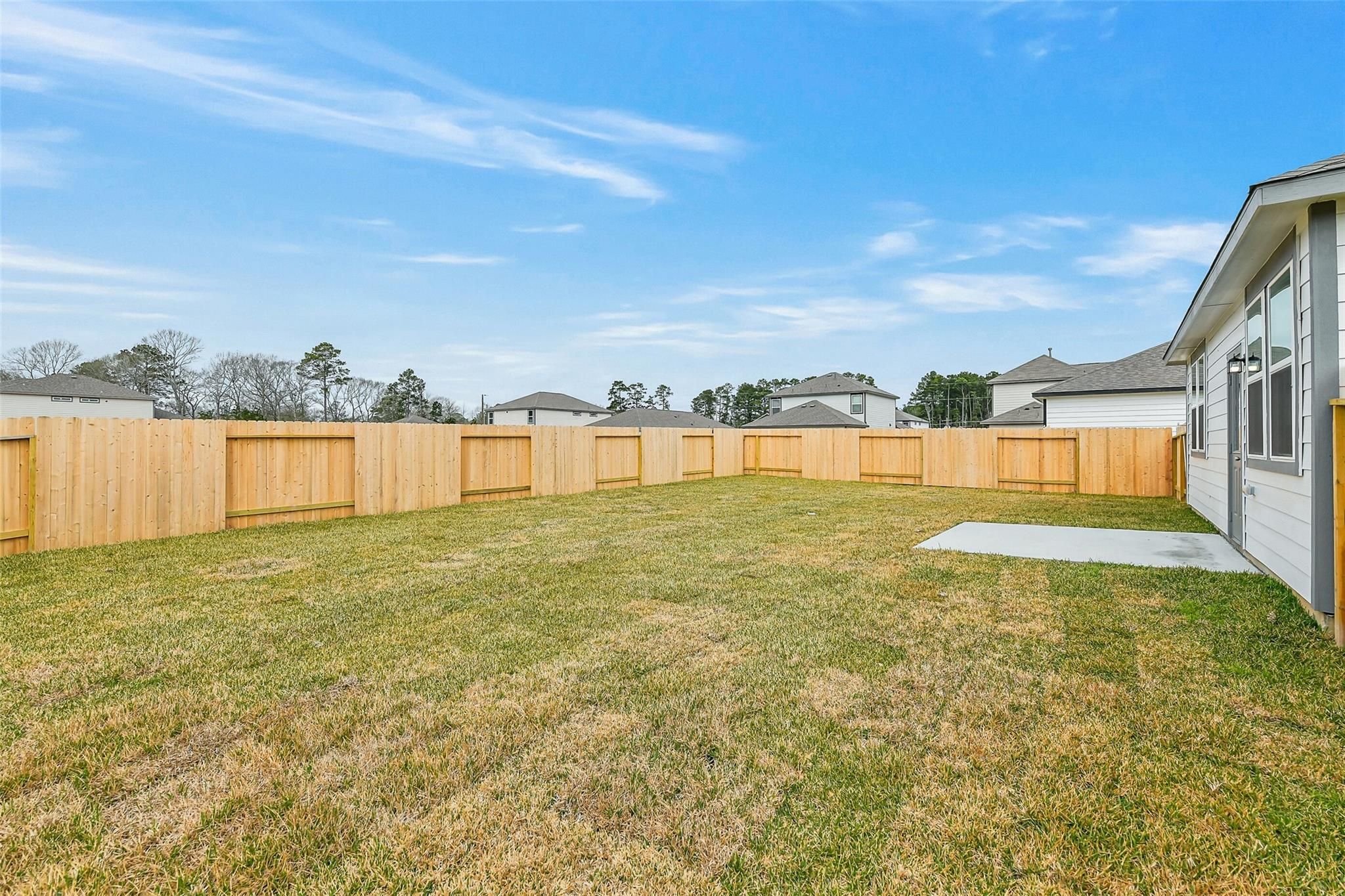Private fenced backyard with green grass and neighboring homes in Davidson Homes The Brazos E, Liberty Estates, Cleveland, Texas