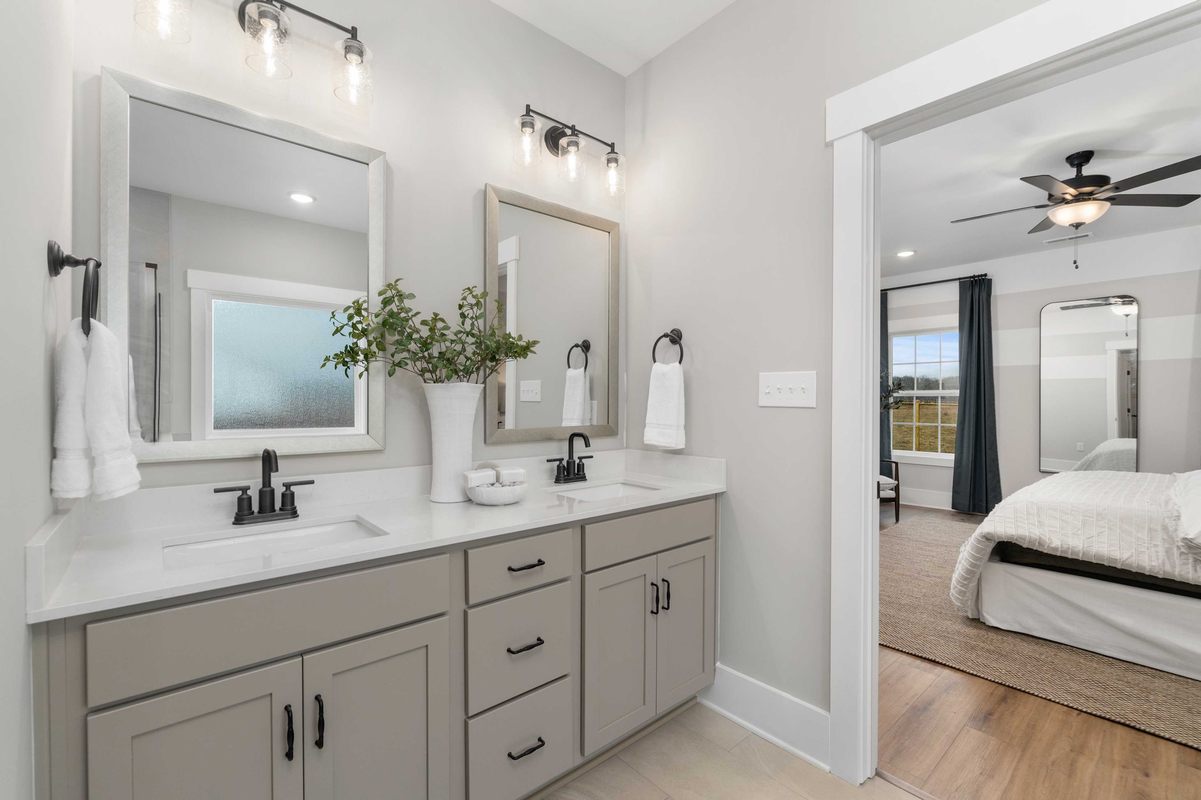 Modern primary bathroom at Kendall Farms in Toney, Alabama with double gray vanity, framed mirrors, and adjacent bedroom view