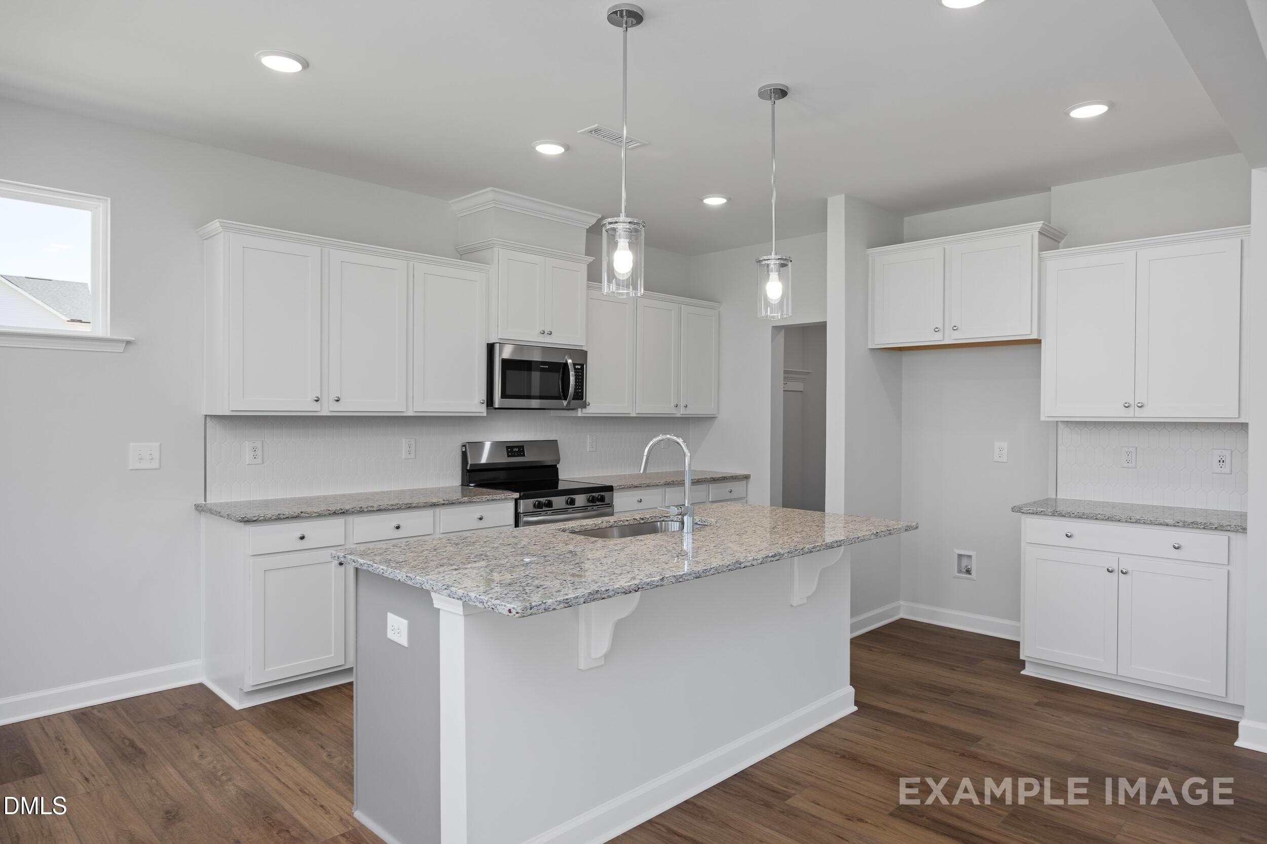 Modern kitchen with white cabinets, granite island, and stainless appliances in The Gavin A floor plan, Gregory Village.