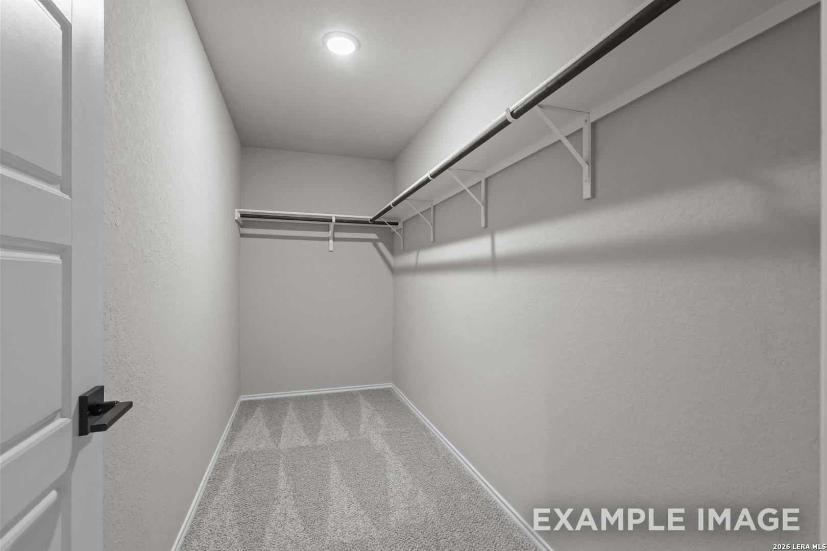 Spacious walk-in closet with dual hanging rods and carpet flooring in Davidson Homes The Murray H plan, Converse, Texas