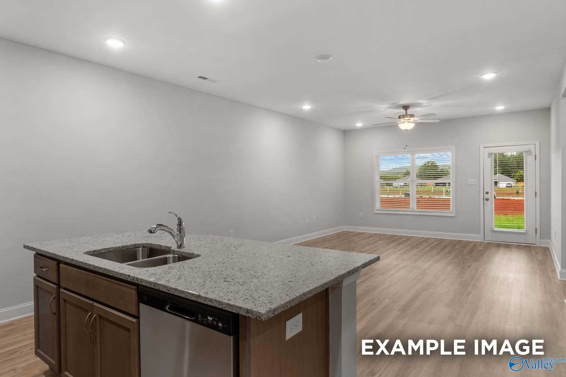 Open-concept kitchen with granite island sink, stainless dishwasher, and wooden cabinets in The Cumberland B home, Decatur, Alabama