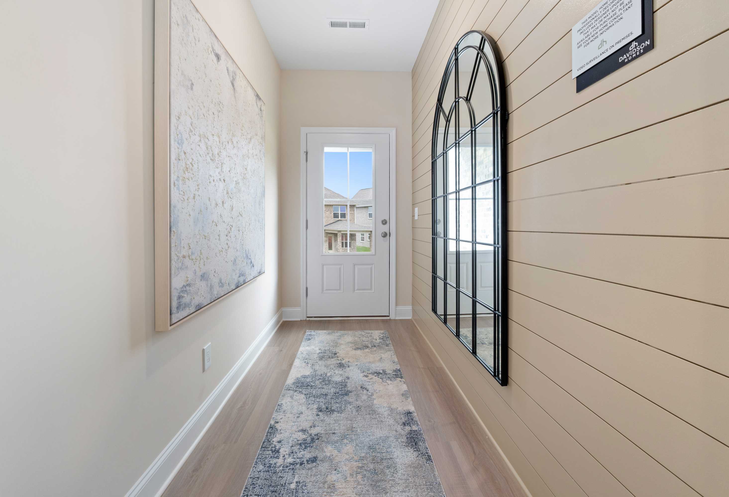 Bright hallway in The Camden home with shiplap walls, arched mirror, abstract wall art, and front door view