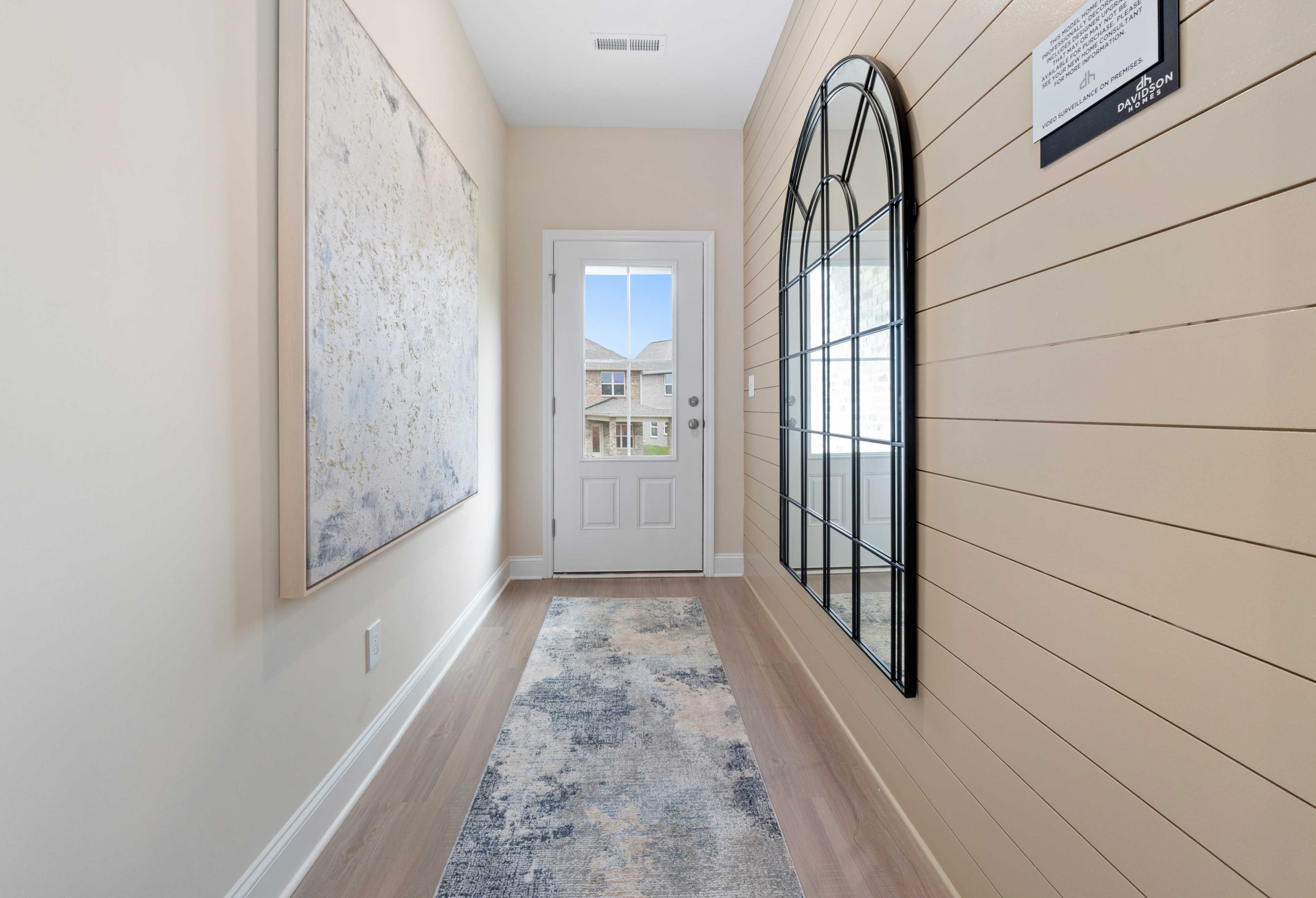 Bright hallway in The Camden home with shiplap walls, arched mirror, abstract wall art, and front door view