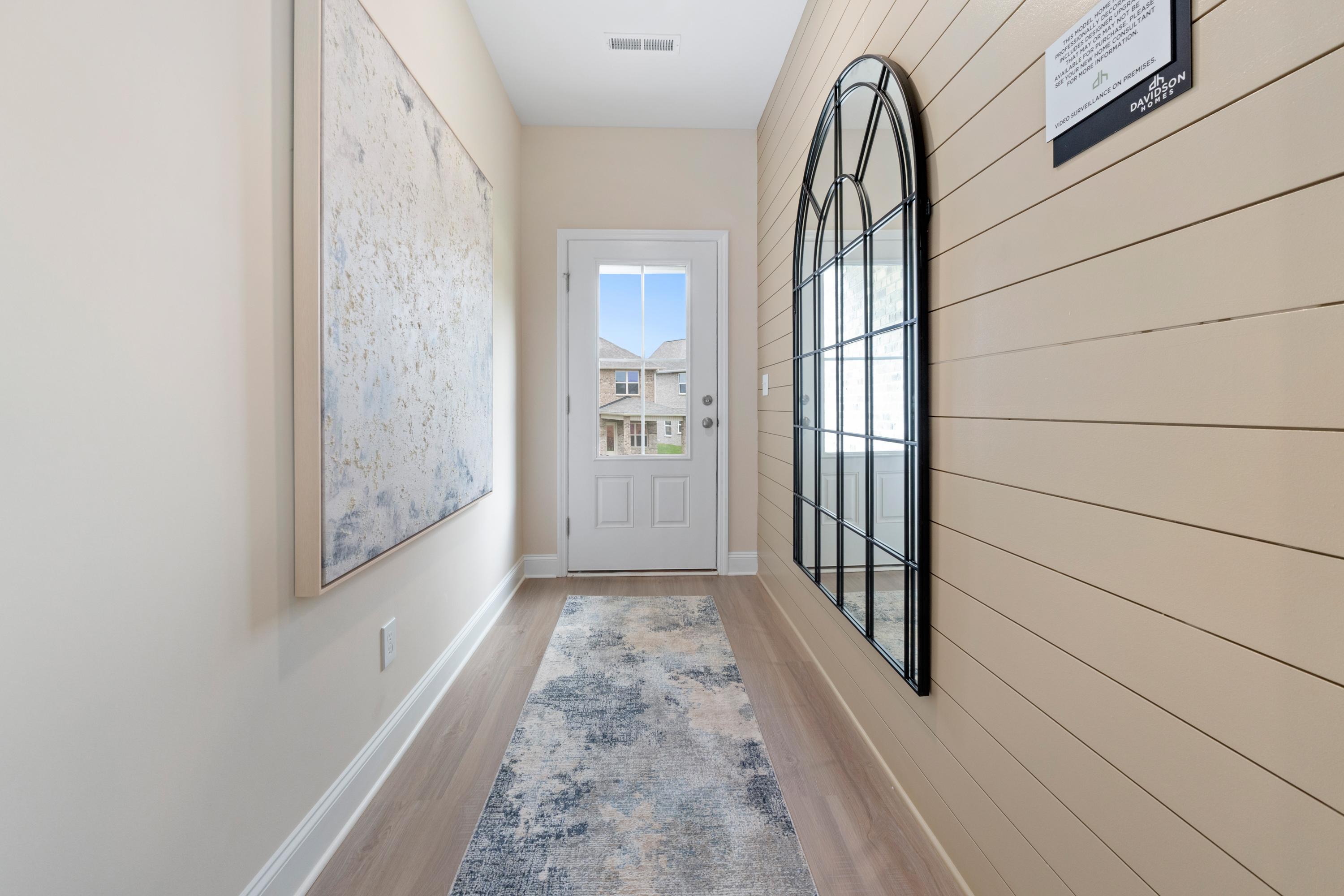 Spacious hallway in Pavilion Huntsville AL with shiplap walls, arched mirror, abstract map art, white door, and hardwood floors