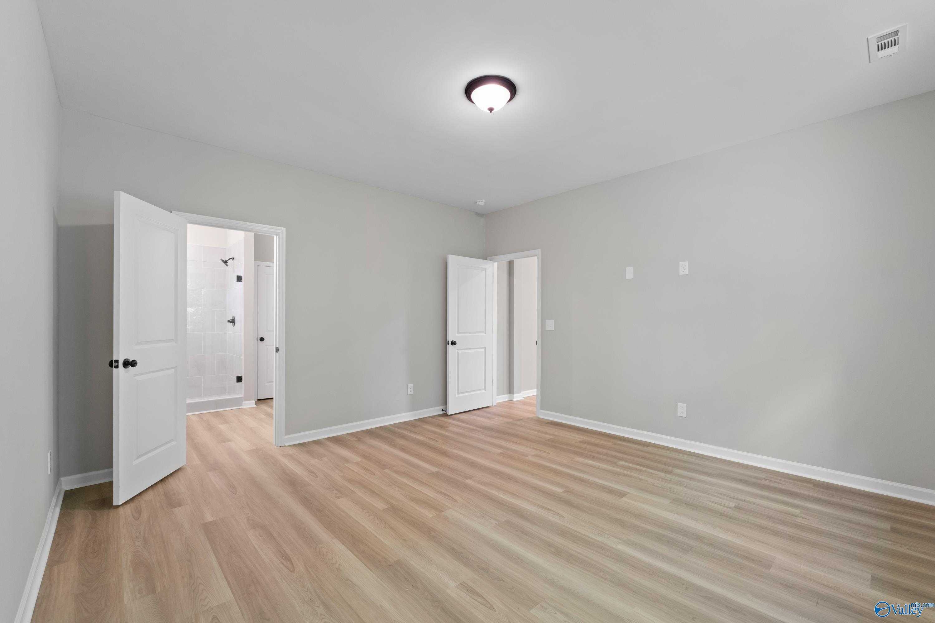 Spacious master bedroom with light gray walls, hardwood floors, and open ensuite bath doors in Davidson Homes The Phoenix, Hazel Green