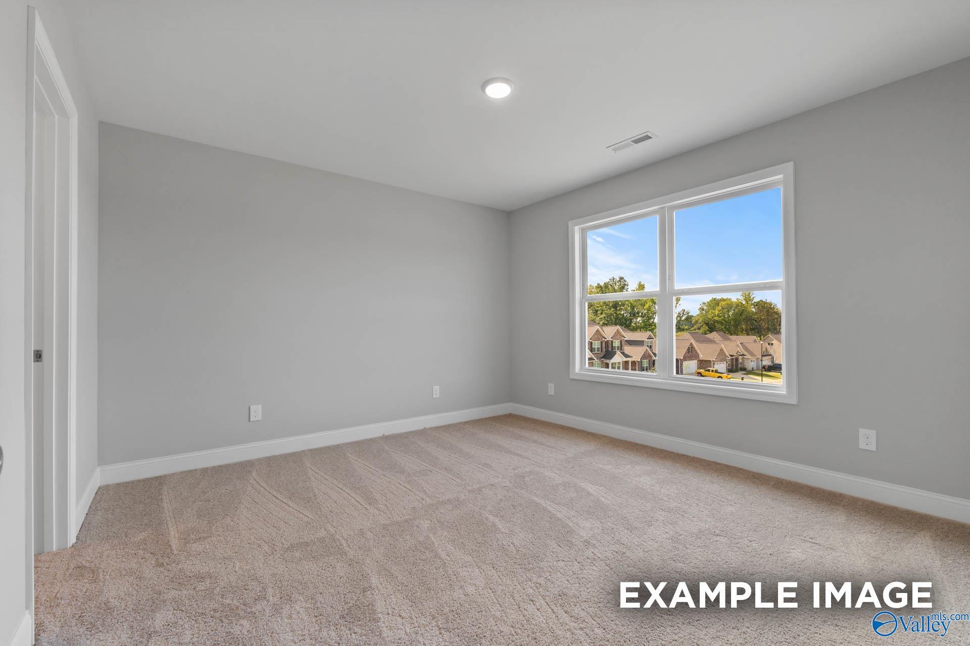 Spacious empty bedroom with gray walls, beige carpet, and large window overlooking neighborhood in Davidson Homes The Shelby B, New Market, Alabama