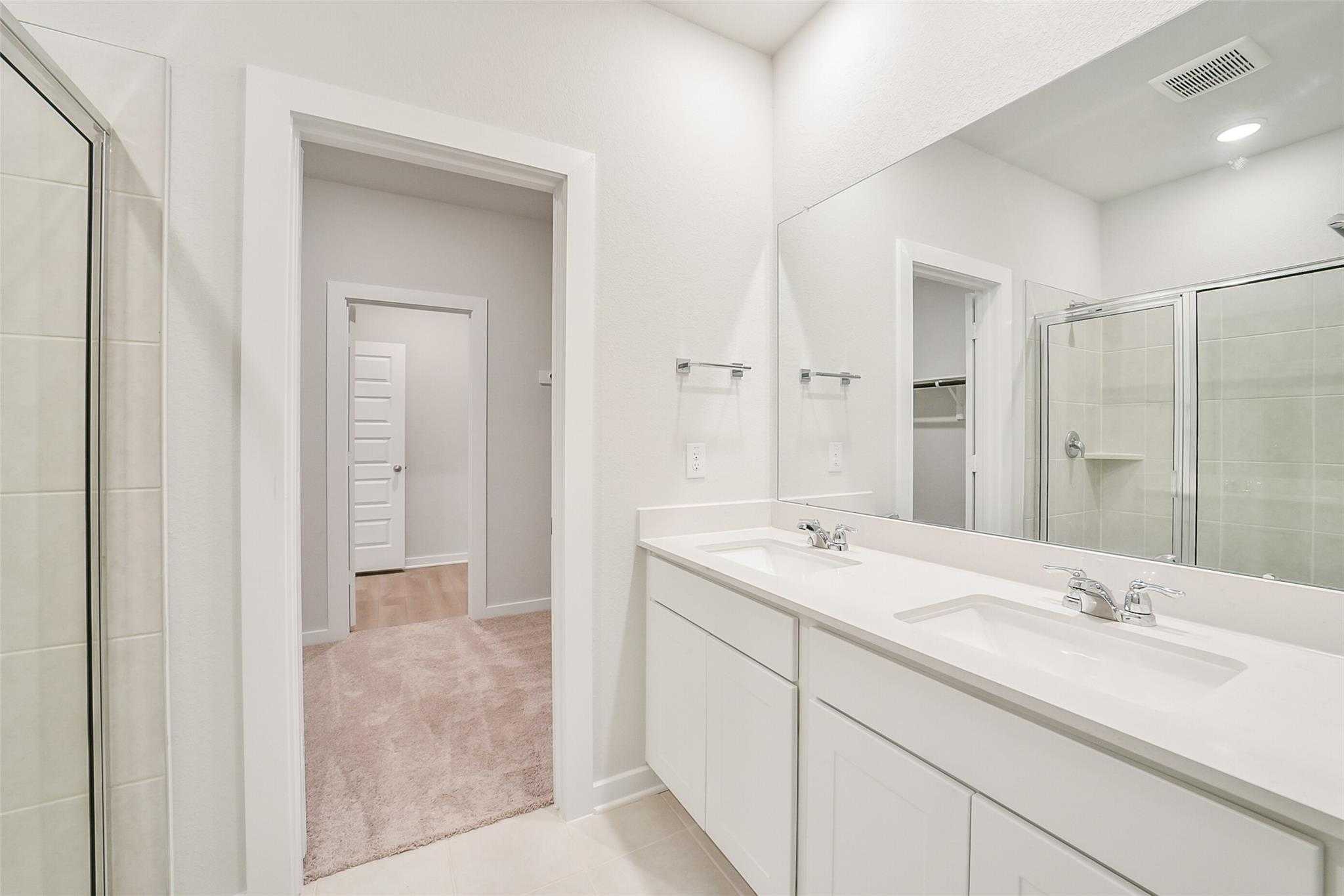 Modern master bathroom featuring double vanity, frameless glass shower, and adjacent closet in Davidson Homes The Blanco E, Magnolia, Texas