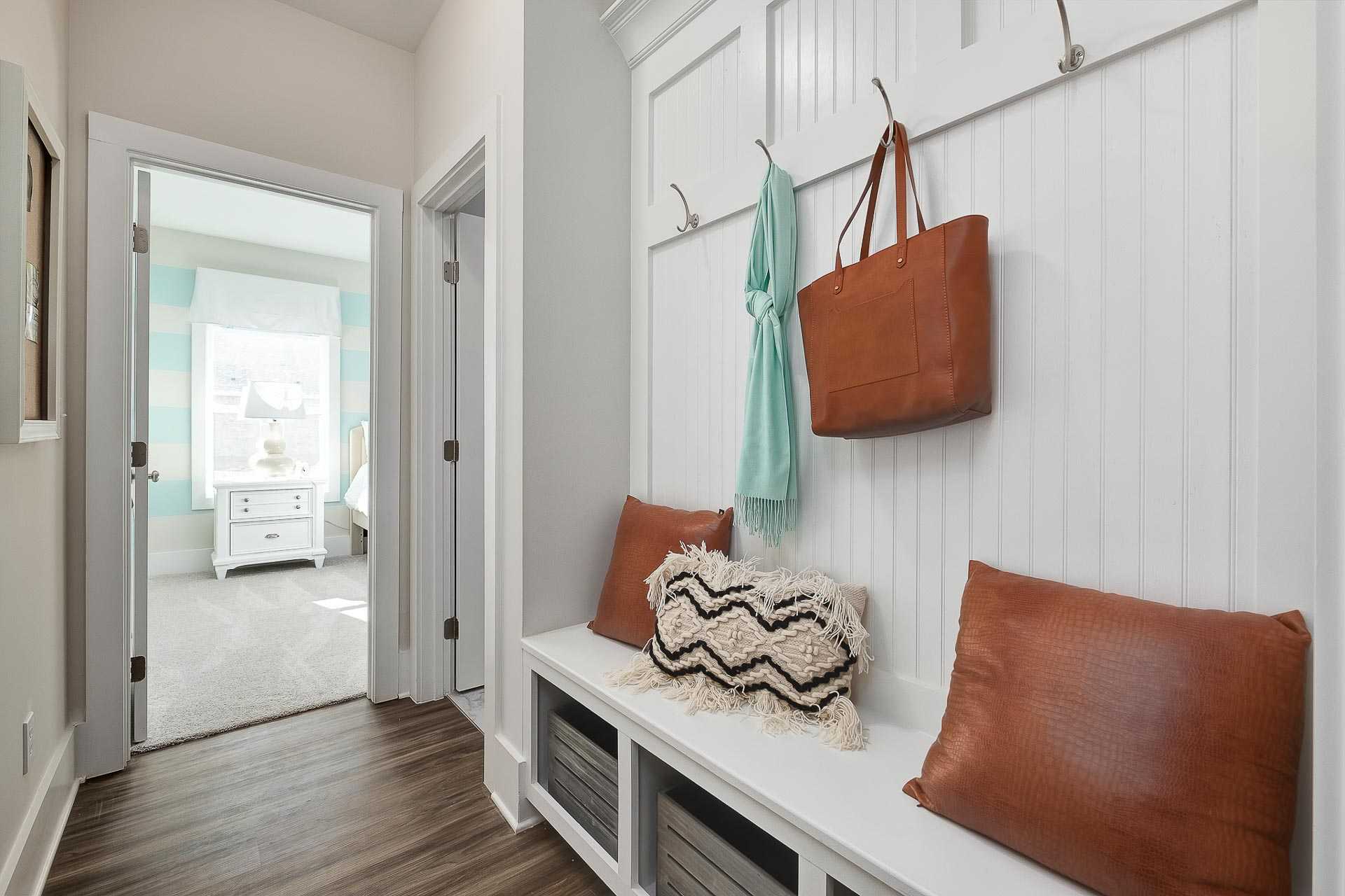 Spacious mudroom with white shiplap walls, built-in bench cushions, coat hooks, scarf and leather bag at Newby Chapel in Athens AL