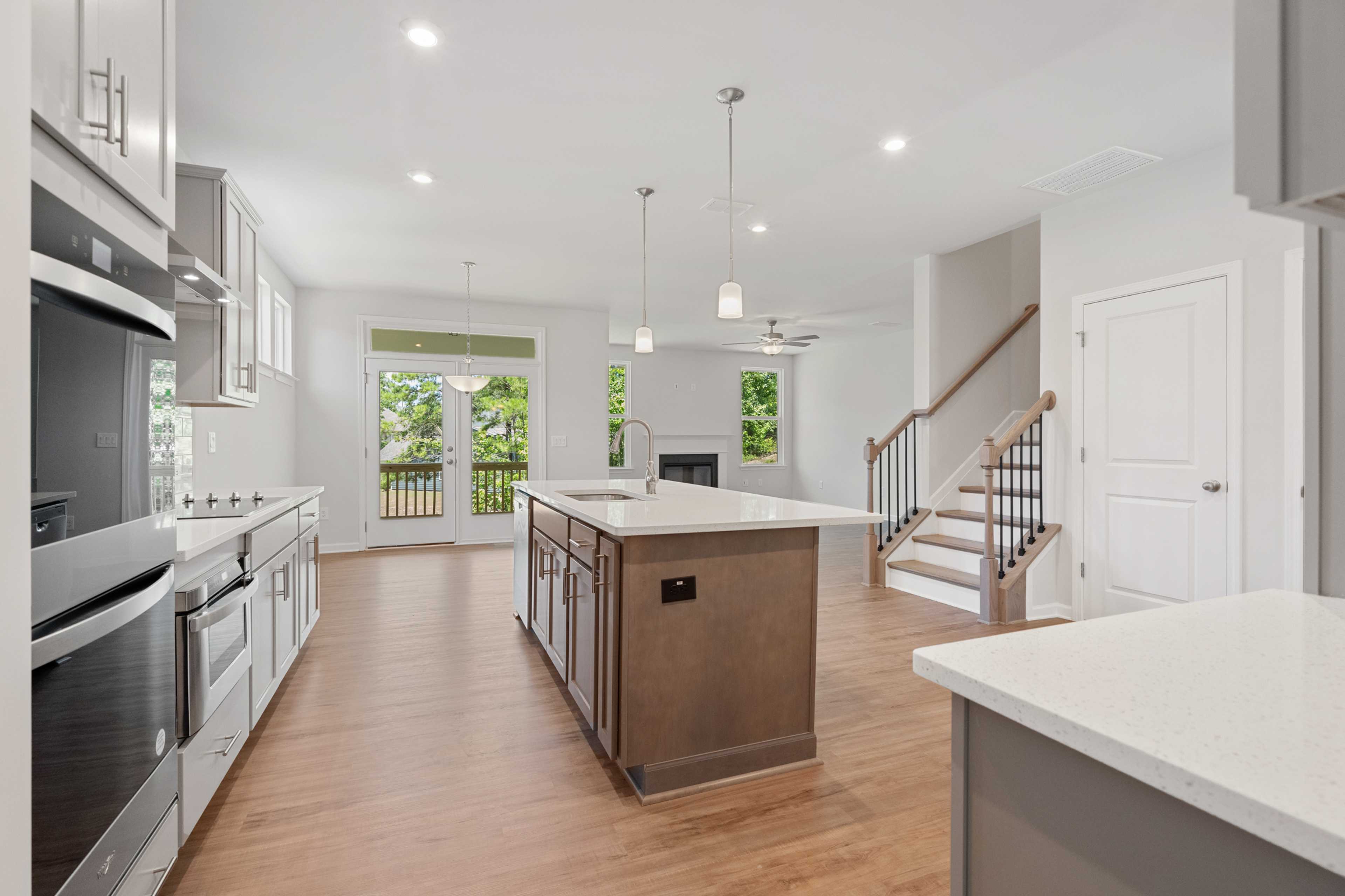 Open-concept kitchen at Mountainbrook in Cartersville GA by Davidson Homes with white cabinets, brown island, hardwood floors, fireplace, and deck access
