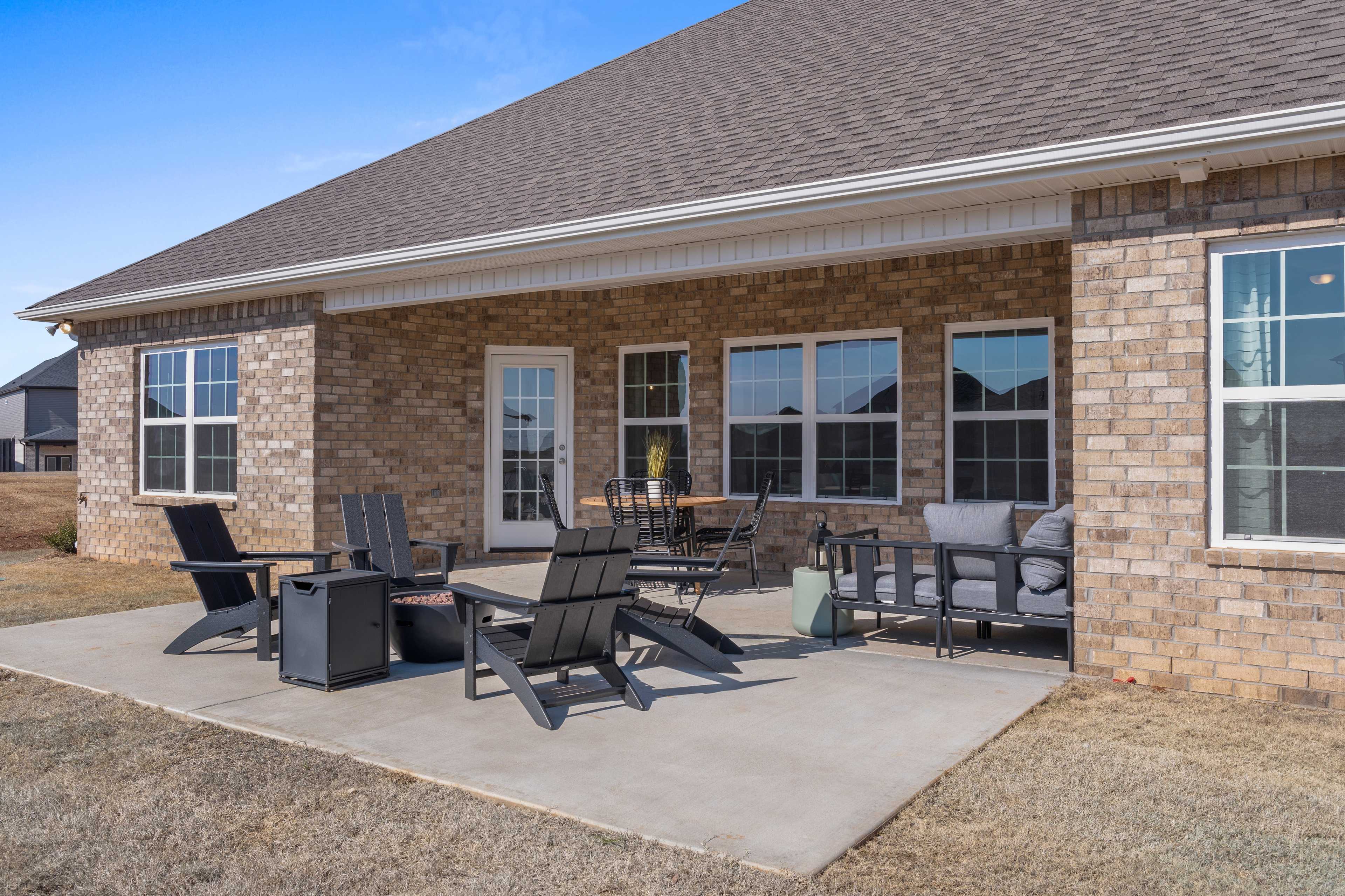 Covered patio with brick home exterior at Barnett's Crossing in Madison, Alabama featuring Adirondack chairs and fire pit table