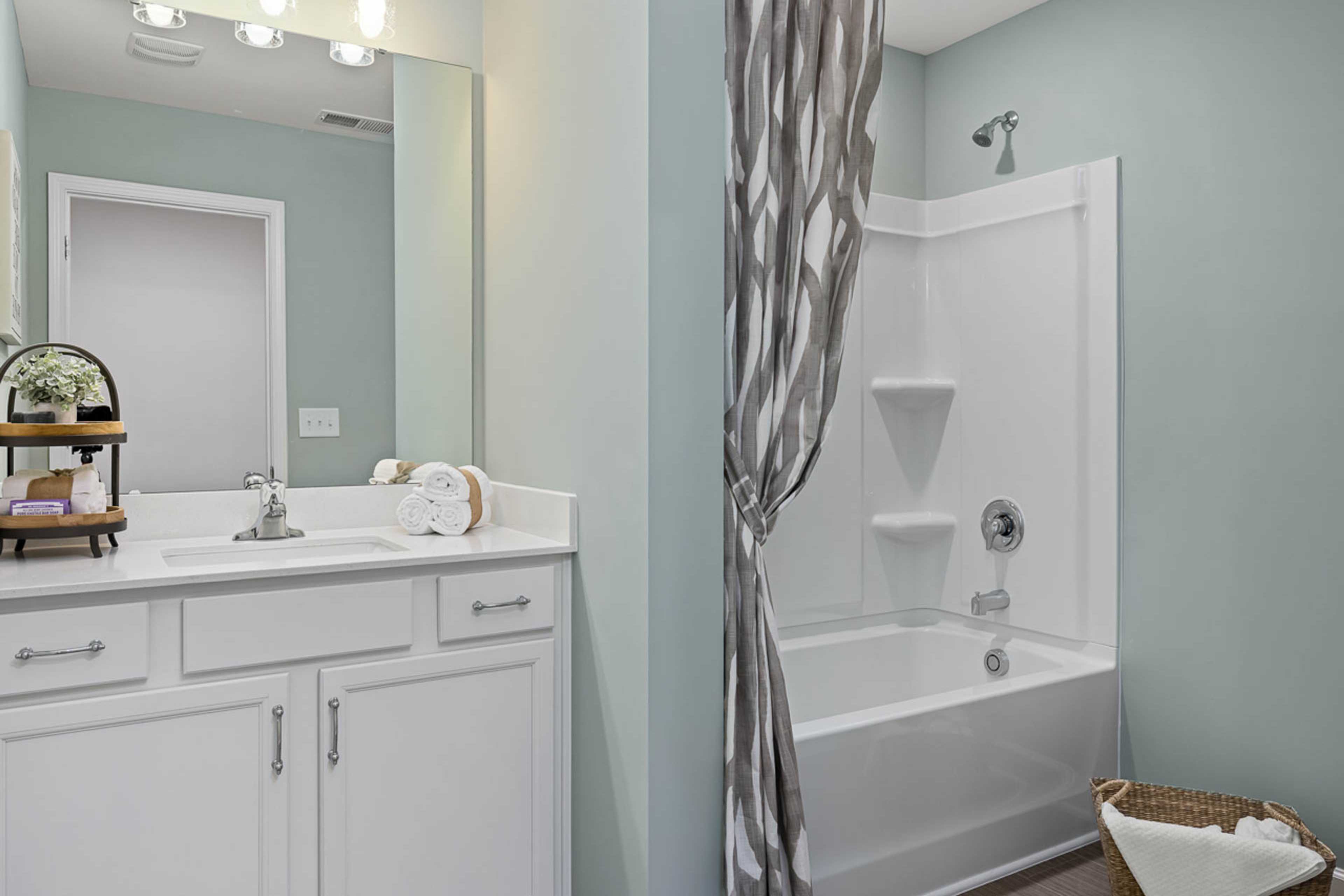 Modern bathroom at Weatherford East in Angier NC with white vanity, gray striped shower curtain, tub combo, and light blue walls