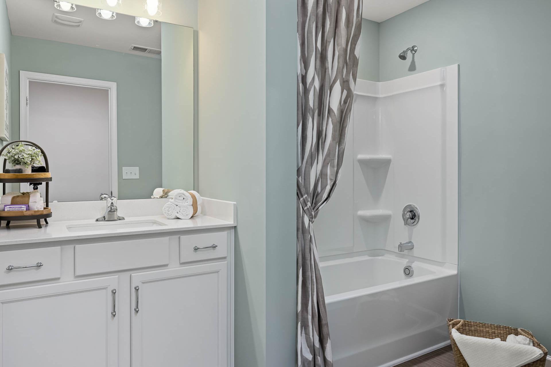 Modern bathroom at Weatherford East in Angier NC with white vanity, gray striped shower curtain, tub combo, and light blue walls