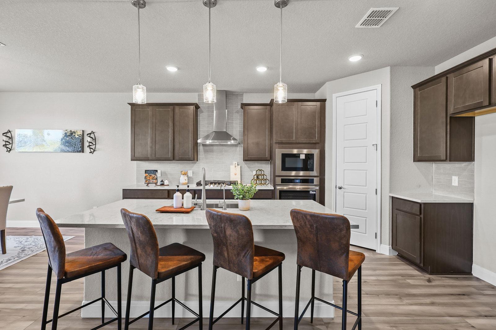 Modern gourmet kitchen in The Jennings G featuring a spacious island, pendant lighting, and dark cabinetry in Castroville, TX.