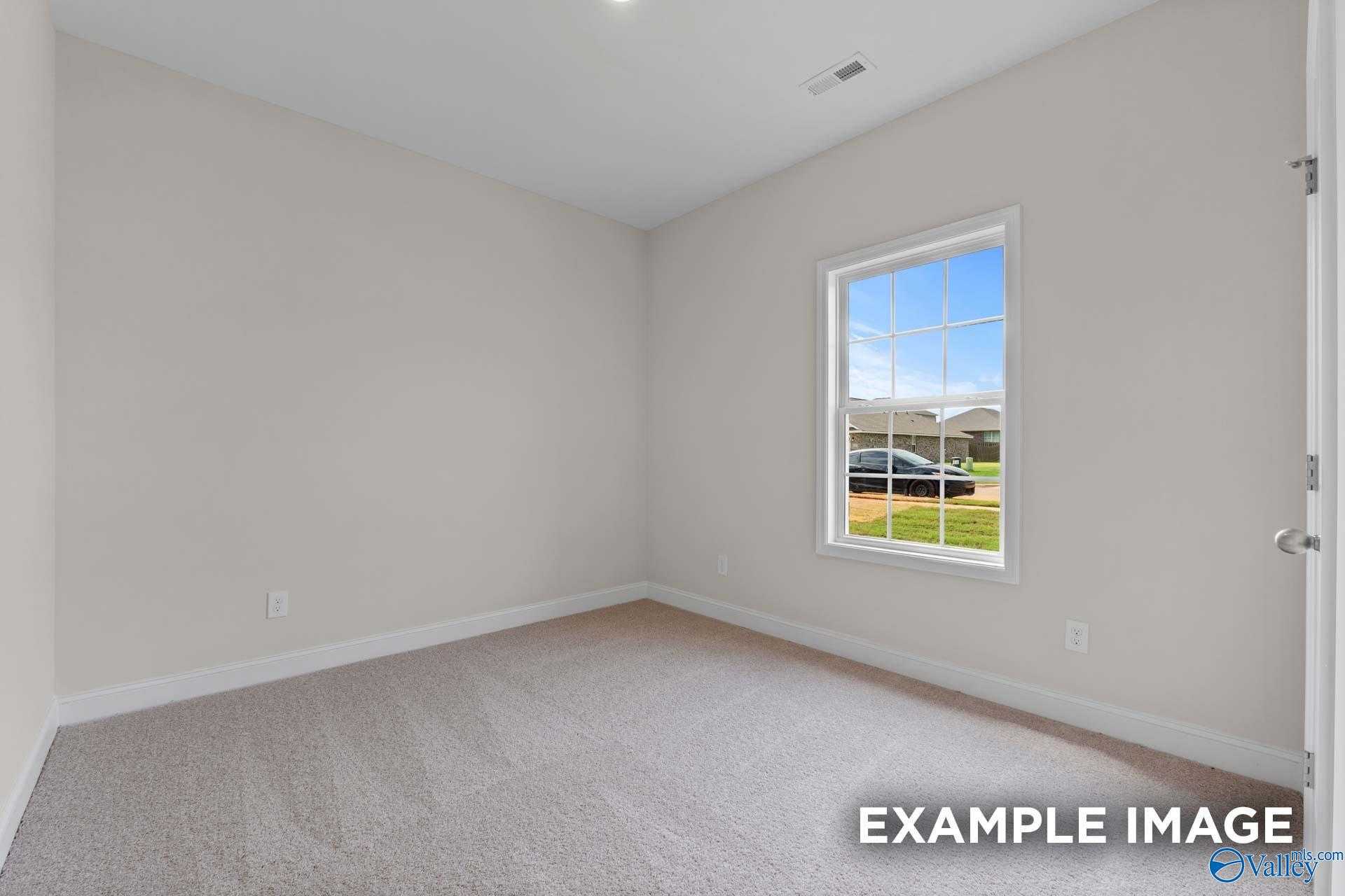 Bright secondary bedroom with neutral walls, carpet flooring, and window view of neighborhood in Davidson Homes The Butler, Toney, Alabama