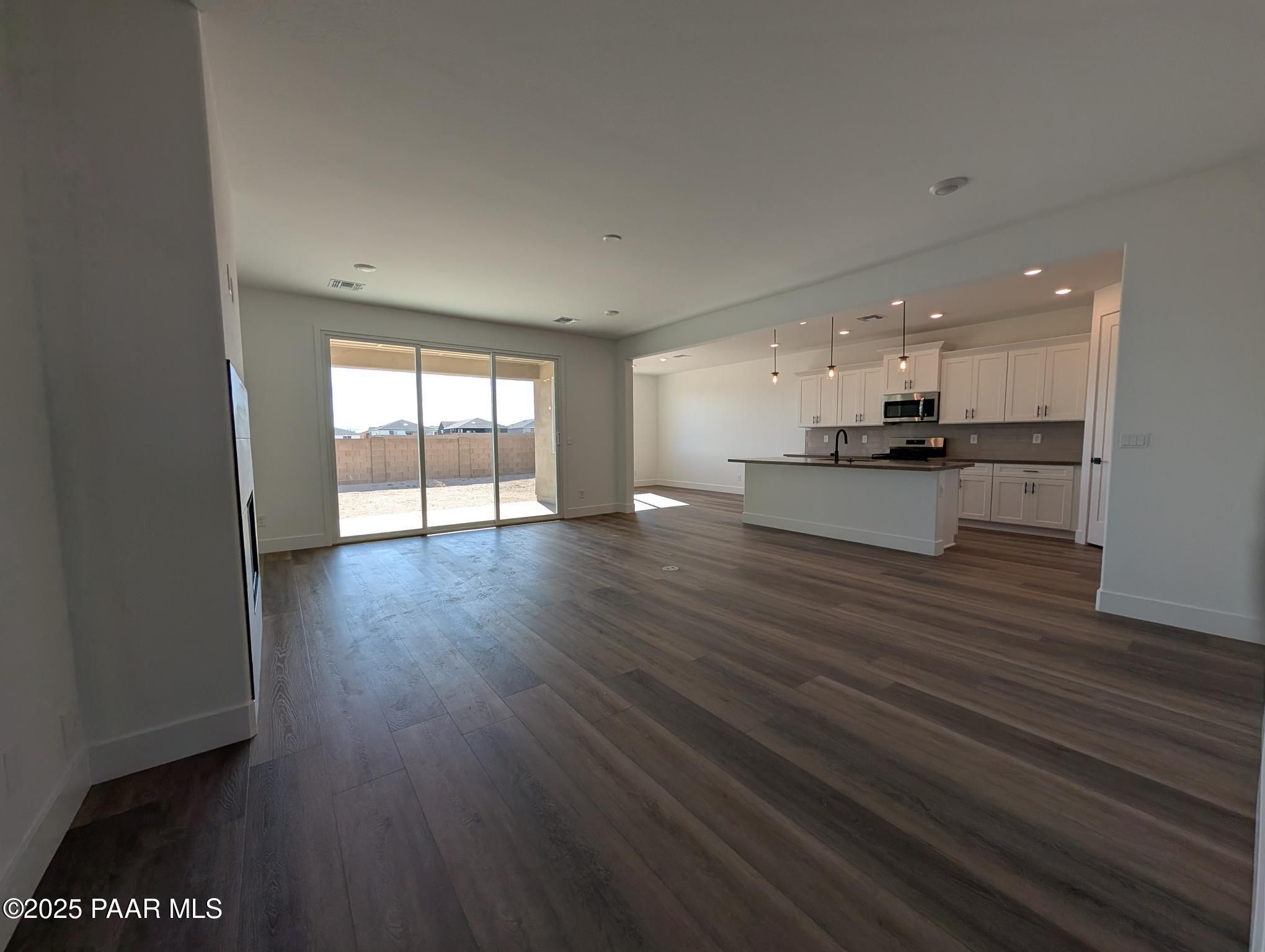Open-concept kitchen and living area with white cabinetry, large island, hardwood floors, and sliding doors to sunny patio in The Sheridan II F, Prescott, AZ