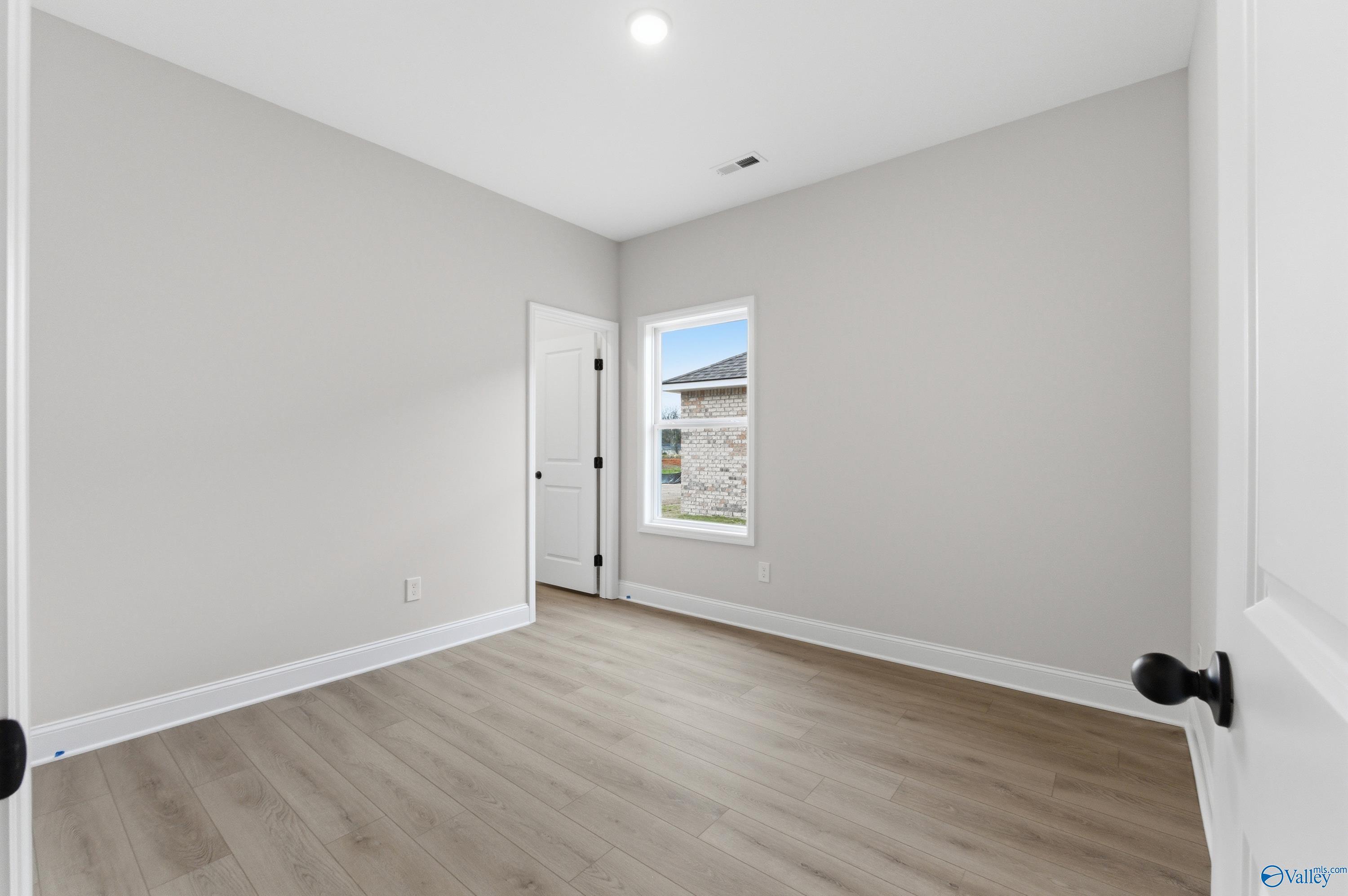 Spacious secondary bedroom with light gray walls, luxury vinyl plank floors, and large window in Davidson Homes The Daphne C, Huntsville