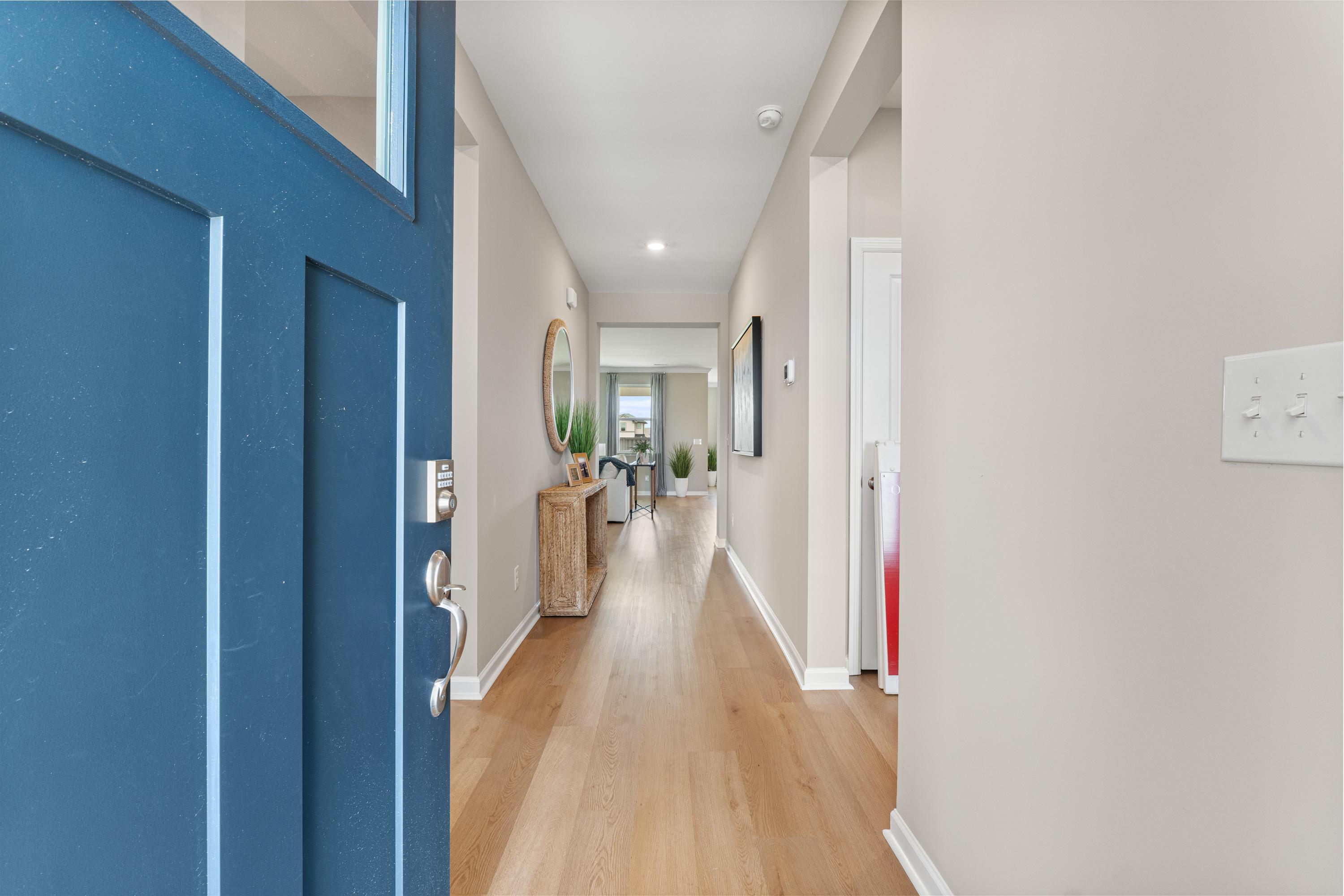 Spacious foyer hallway at The Meadows at Hampton Cove in Owens Cross Roads AL with oak hardwood floors, open blue door, and round mirror