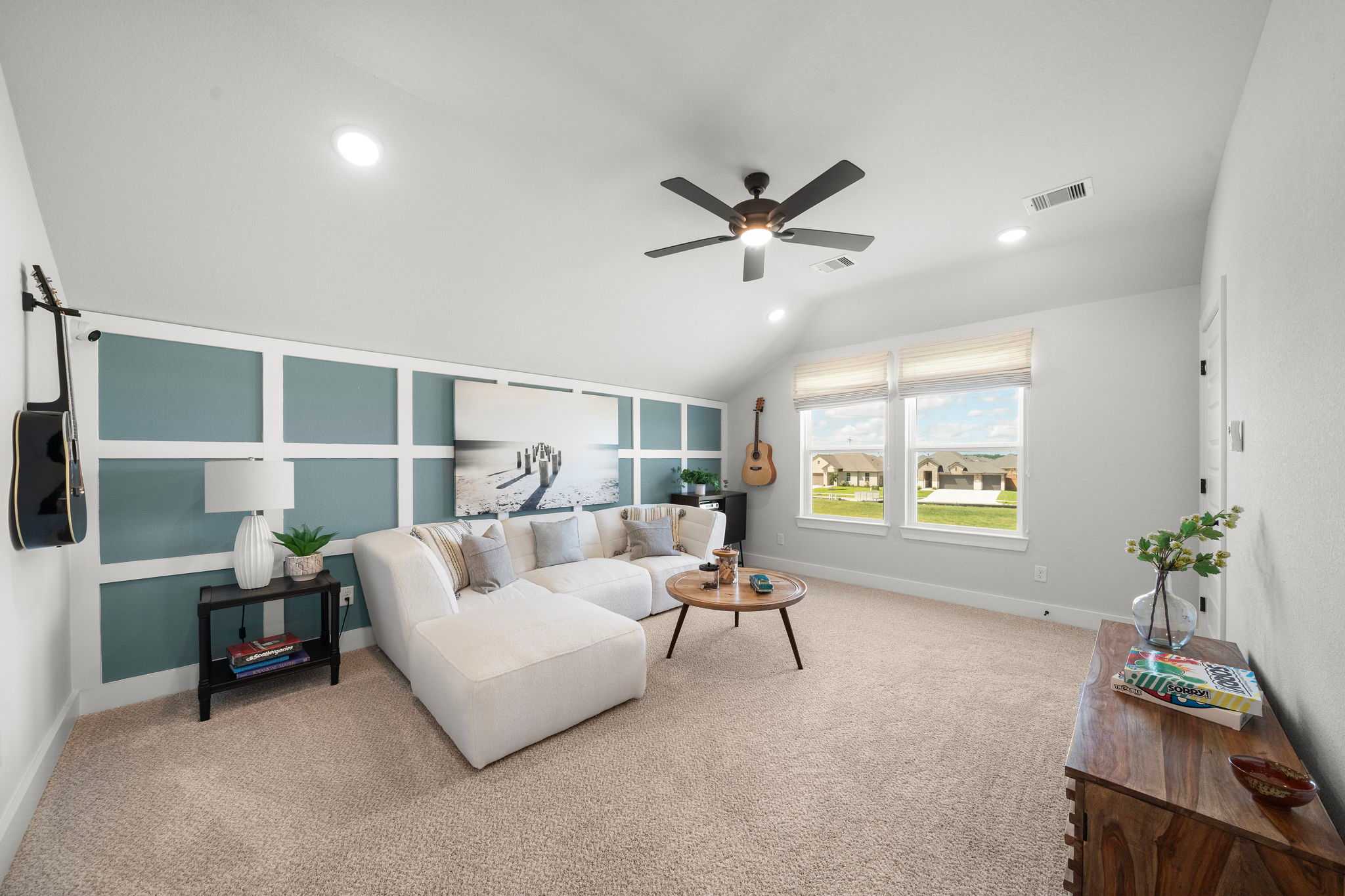 Spacious loft game room at Lago Mar in Texas City TX by Davidson Homes with white L-shaped sofa, ceiling fan, and guitar wall accents