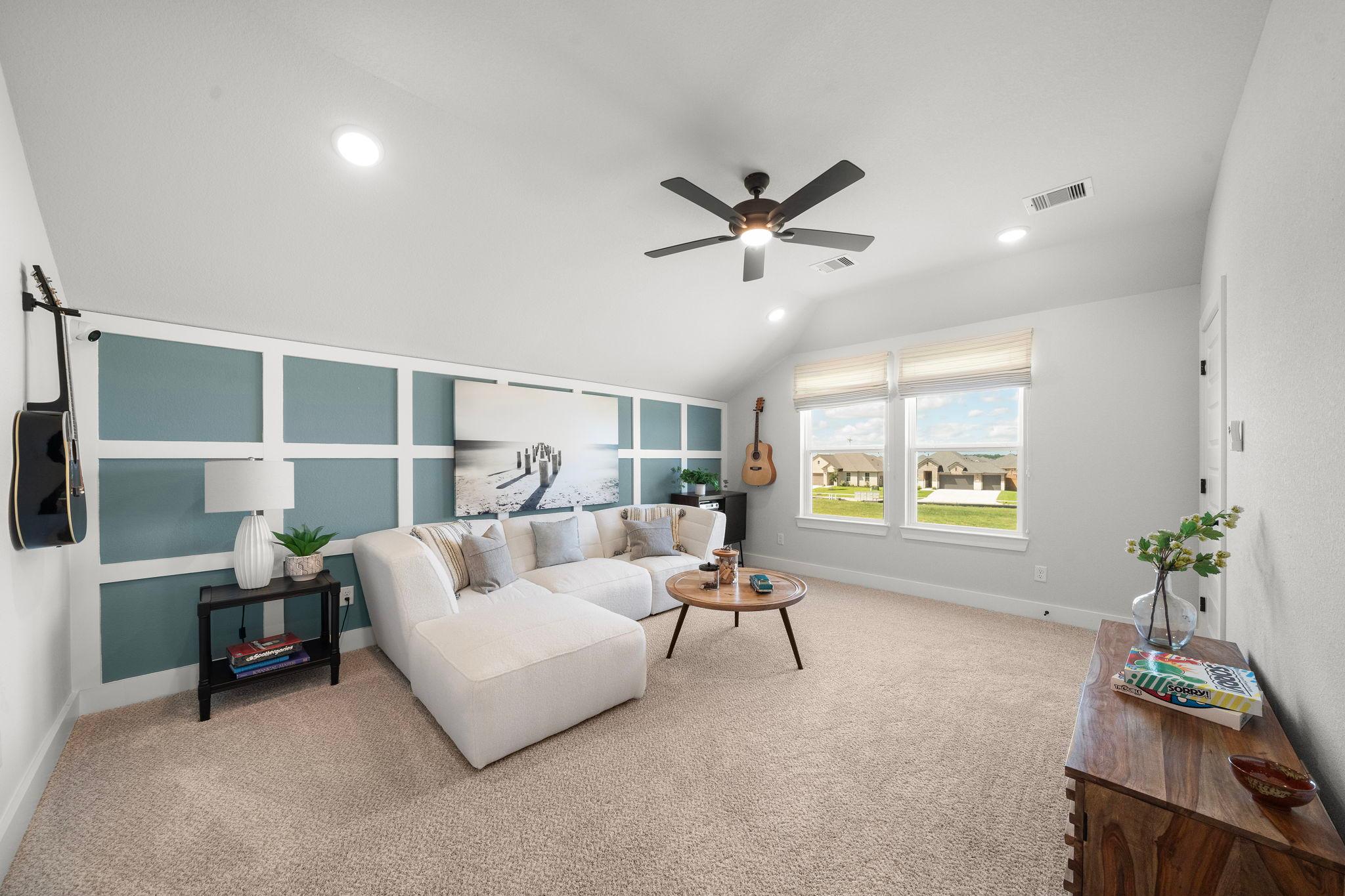 Spacious loft game room at Lago Mar in Texas City TX by Davidson Homes with white L-shaped sofa, ceiling fan, and guitar wall accents
