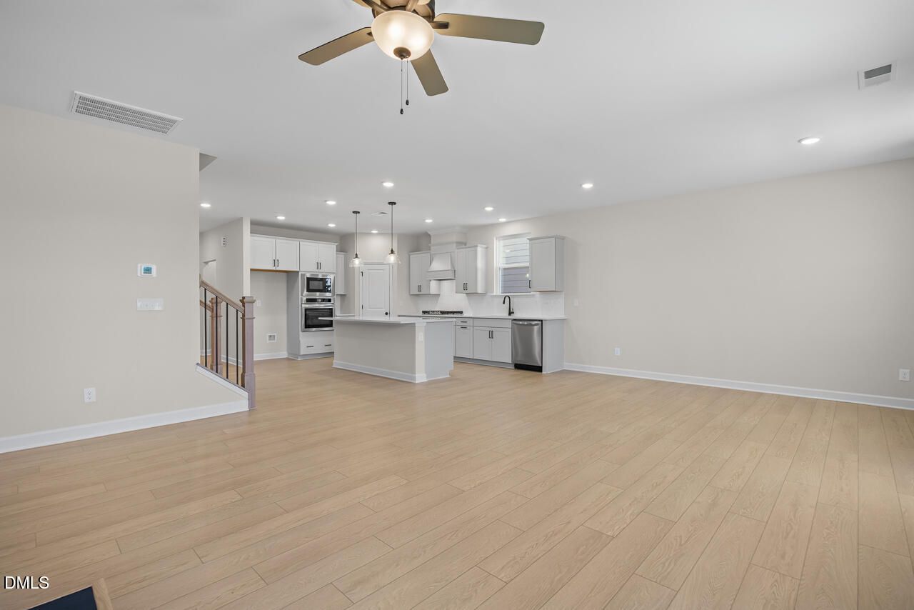 Open-concept living room and kitchen with white cabinetry and light wood floors in Davidson Homes The Ashport M, Wendell NC