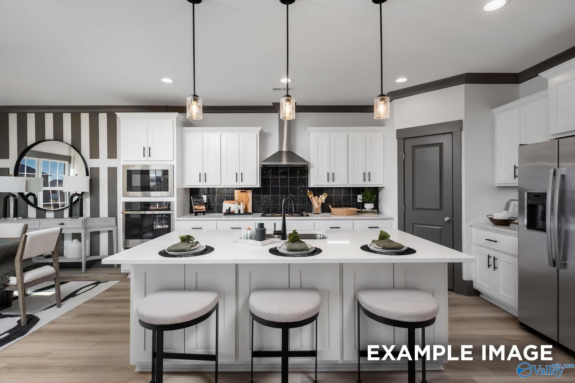 Modern white kitchen island with bar stools, stainless appliances, and pendant lights in Davidson Homes The Rockford B, Madison, AL