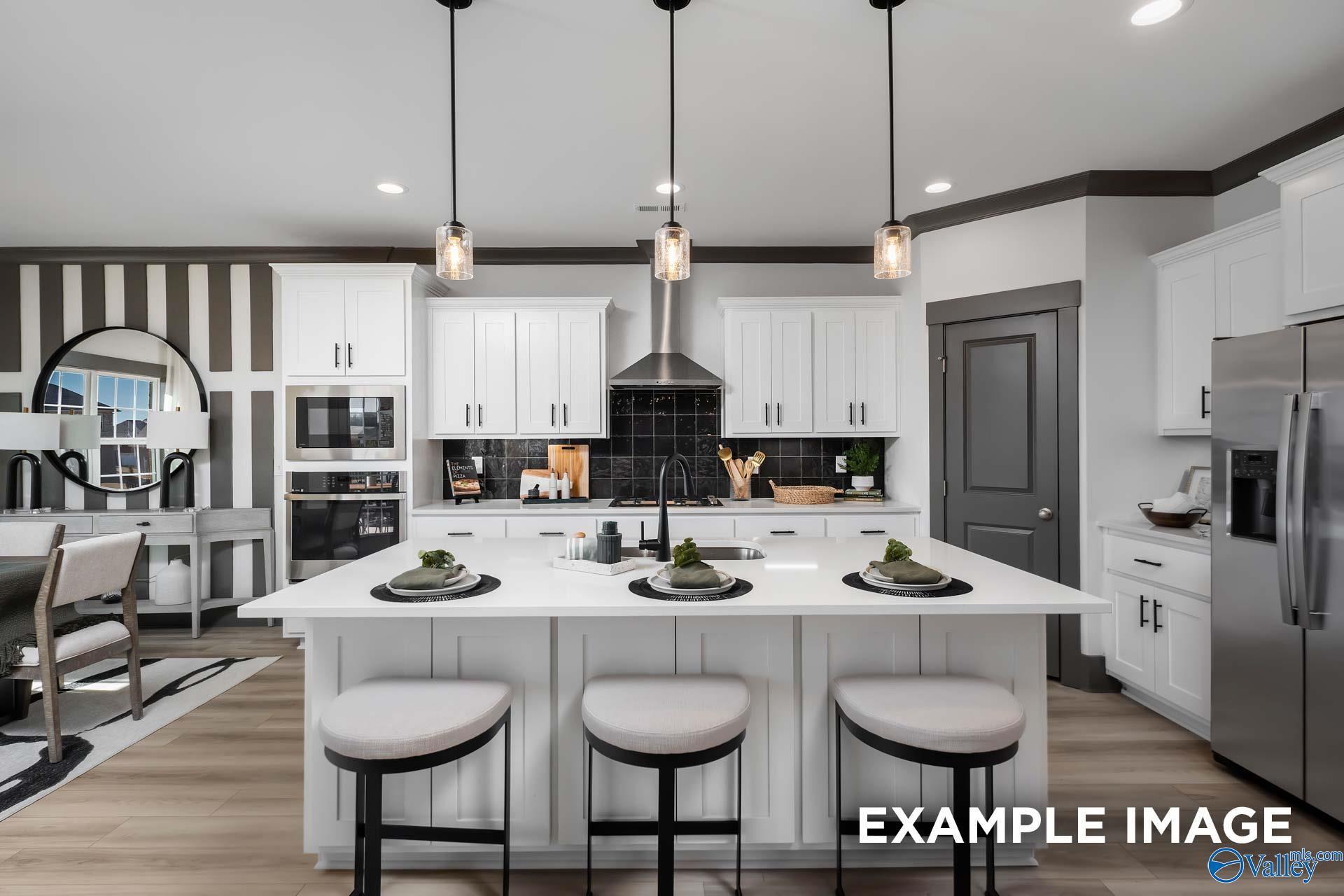 Modern white kitchen island with bar stools, stainless appliances, and pendant lights in Davidson Homes The Rockford B, Madison, AL