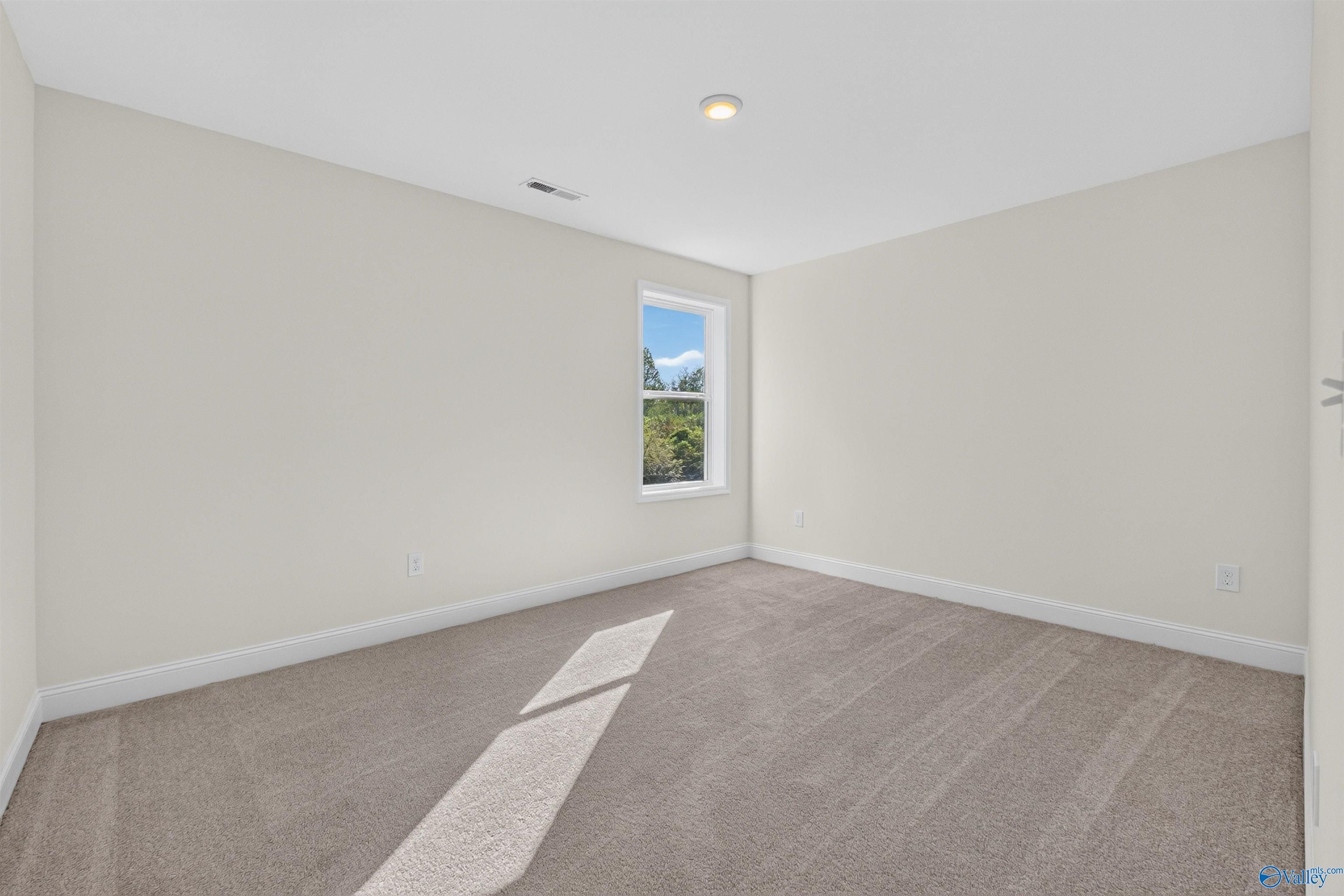 Bright empty bedroom with neutral walls, carpet flooring, and sunny window in Davidson Homes Ashport L plan, Berry Cove, AL