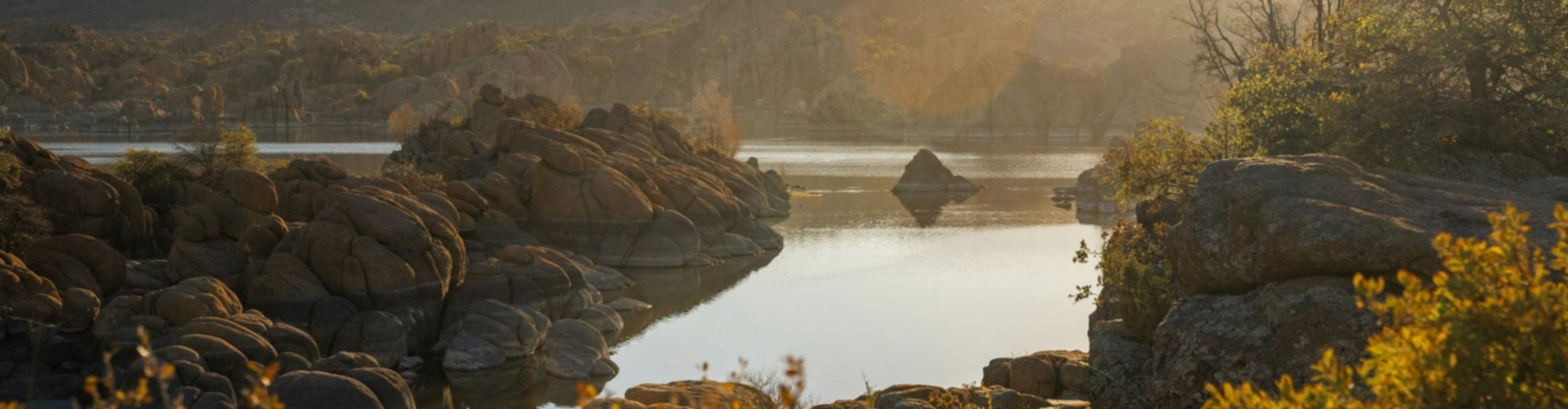 Golden sunset over rocky Prescott lake with autumn foliage and distant mountains