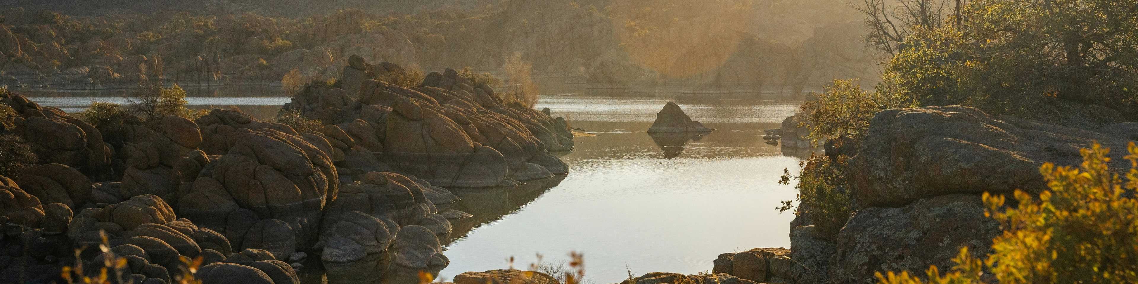 Golden sunset over rocky Prescott lake with autumn foliage and distant mountains