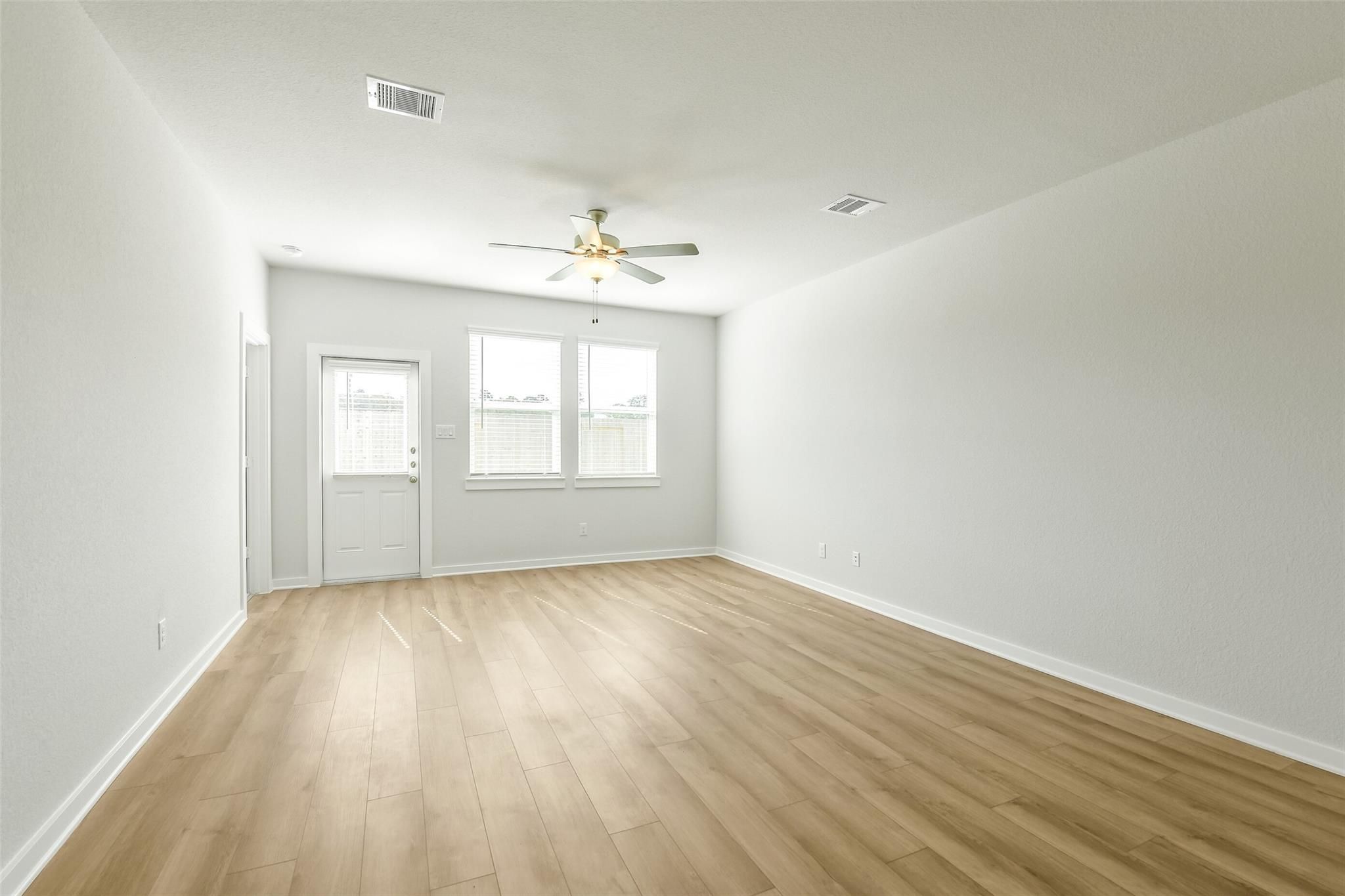Spacious empty upstairs room with light hardwood floors, white walls, ceiling fan, and large windows in Davidson Homes San Marcos E, Cleveland, Texas